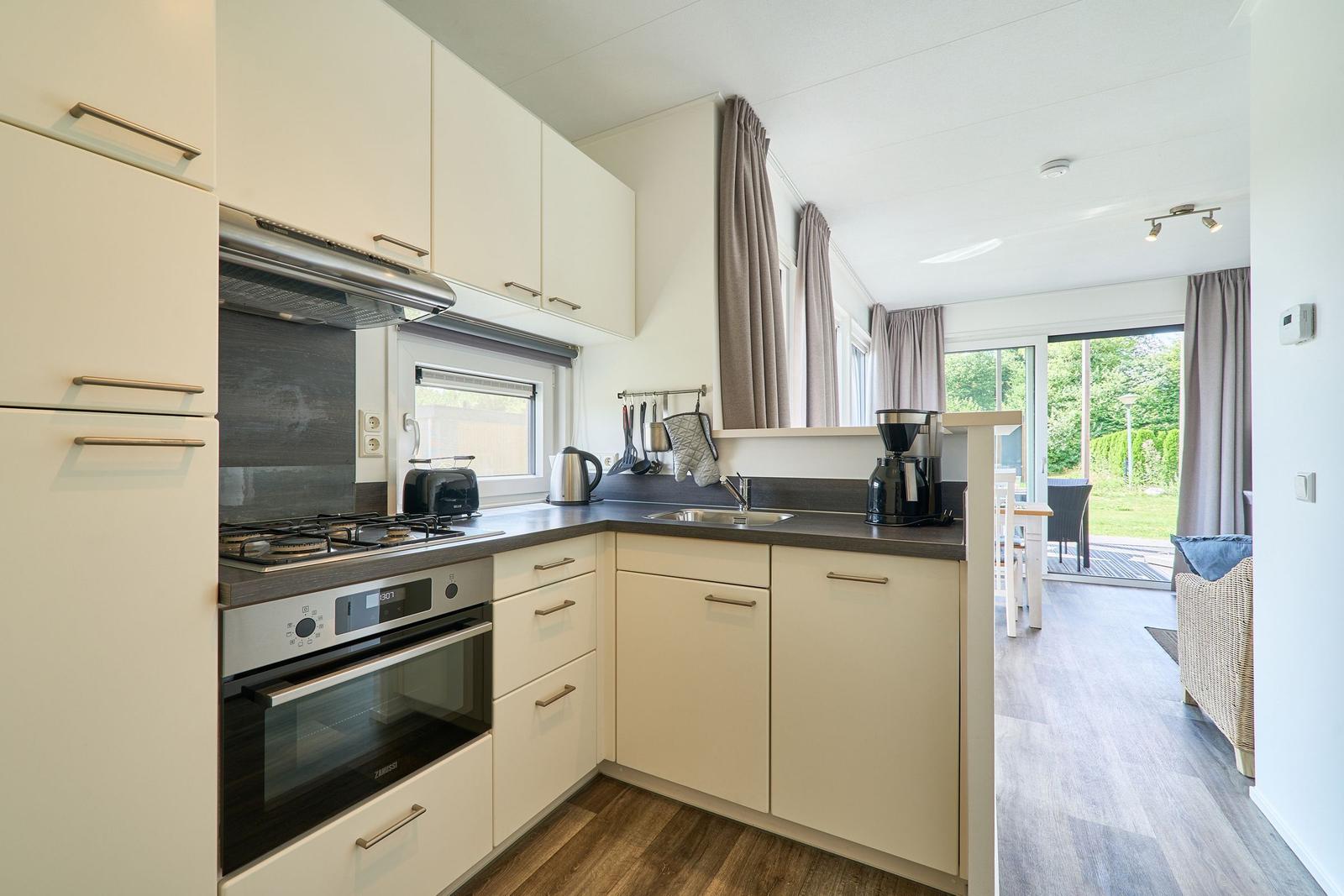 Küche mit weißen Schränken, Edelstahlherd und Blick auf Terrasse.