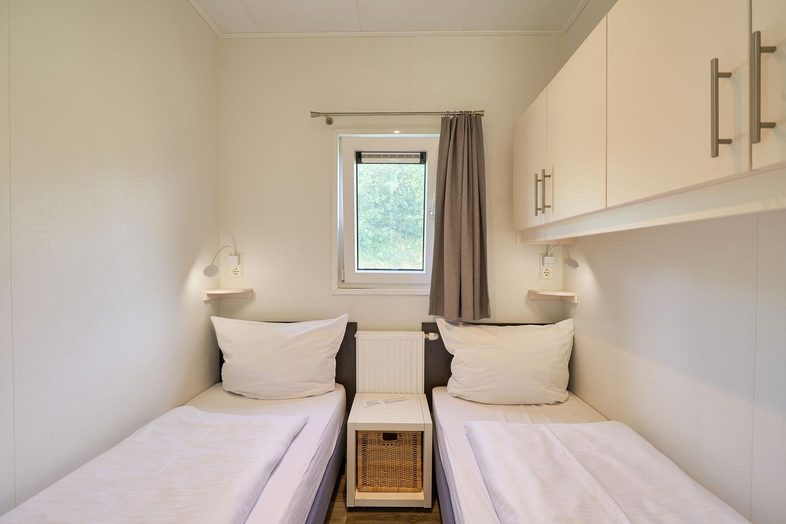 Zwei Einzelbetten mit weißen Bettwäschen, kleiner Nachttisch und Fenster mit Vorhang.