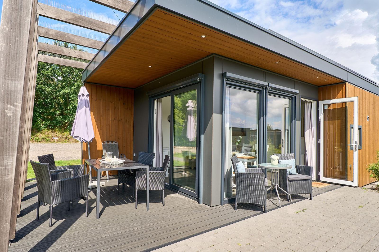 Terrasse mit Sitzgruppe und Tisch unter Holzüberdachung. Glasfront öffnet sich zum Innenraum.