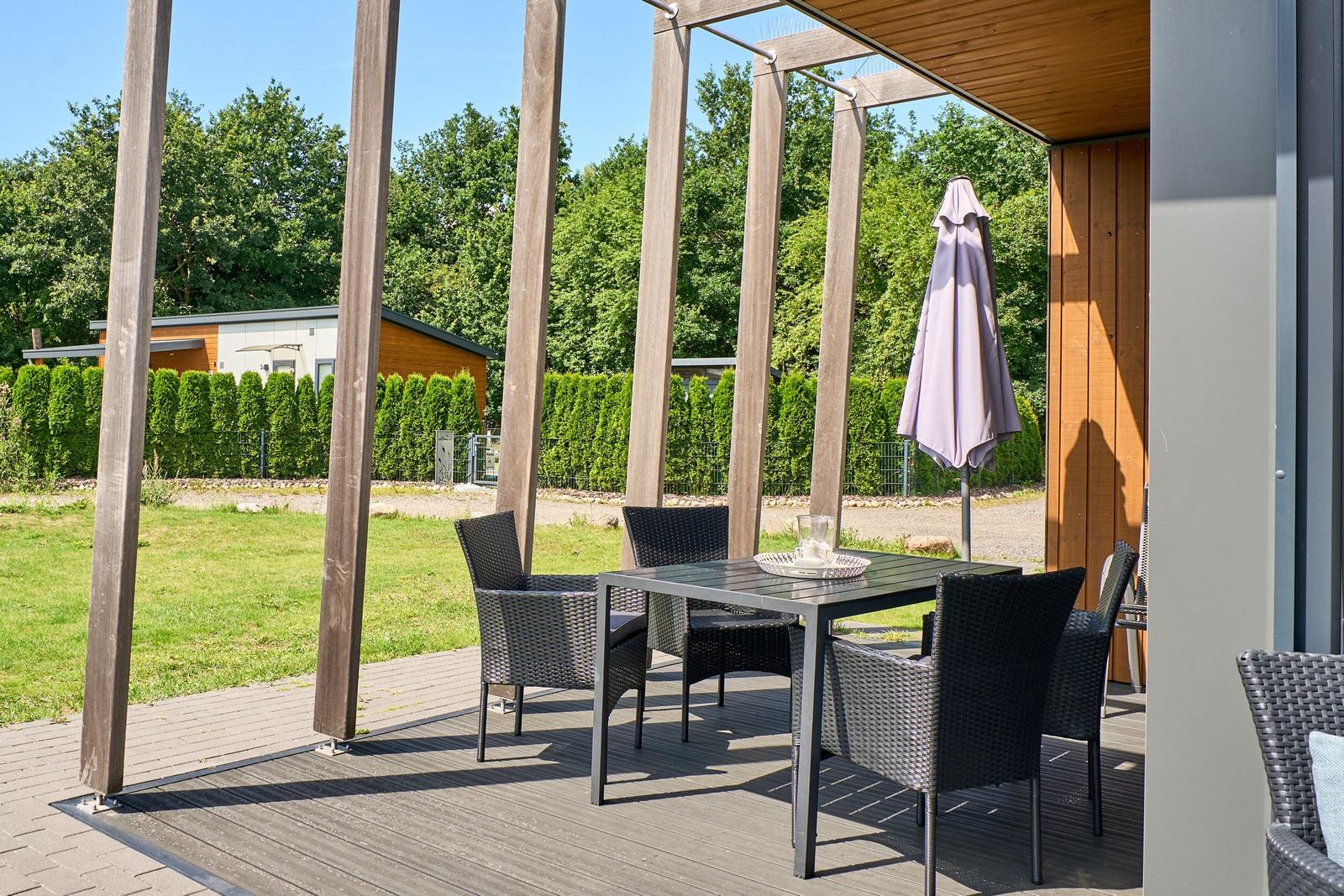 Terrasse mit Tisch und Stühlen unter Pavillon. Hintergrund: Gras, Bäume und Hecke.