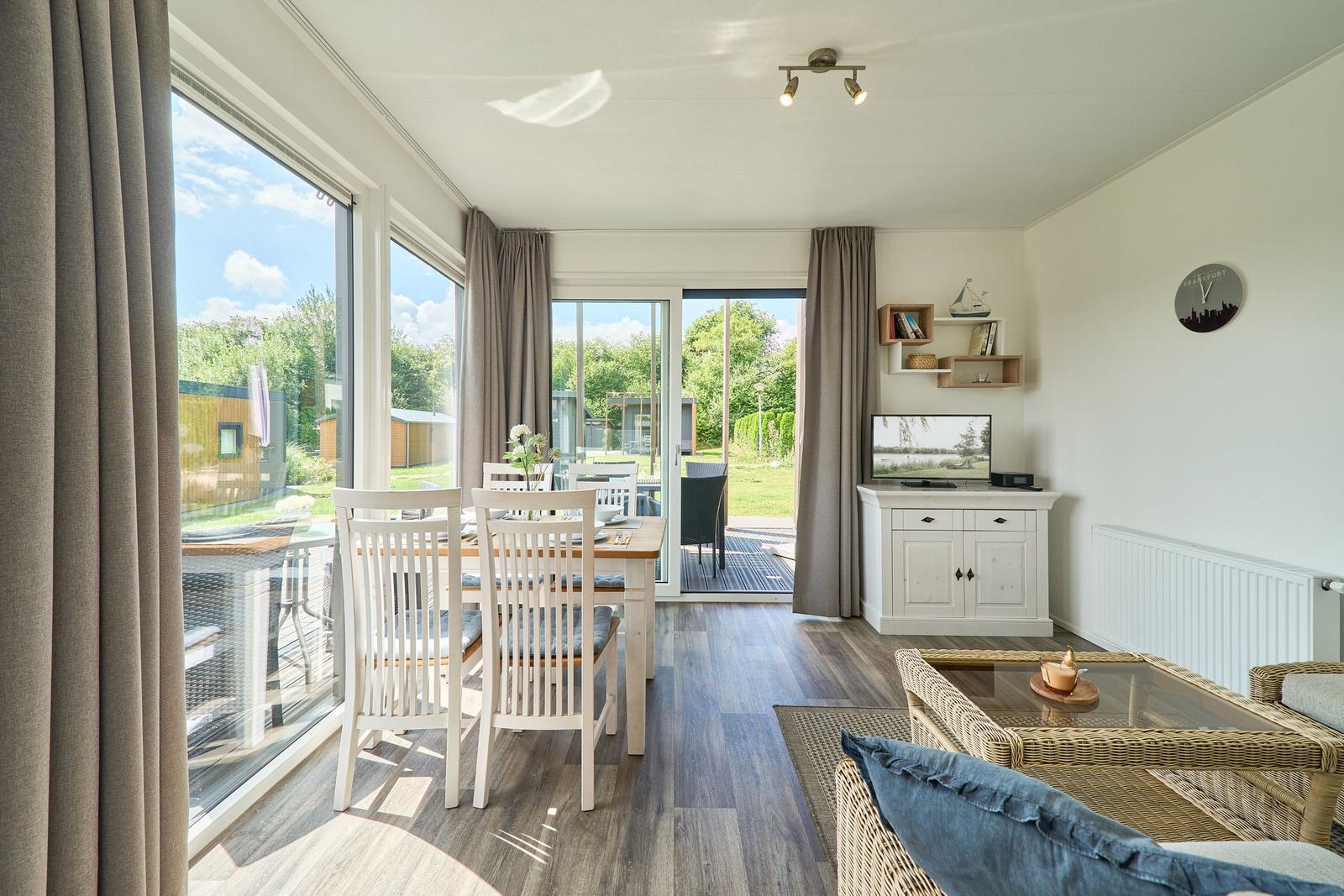 Wohn- und Essbereich mit großem Fenster und Terrasse. Möbel aus Holz und Rattan.