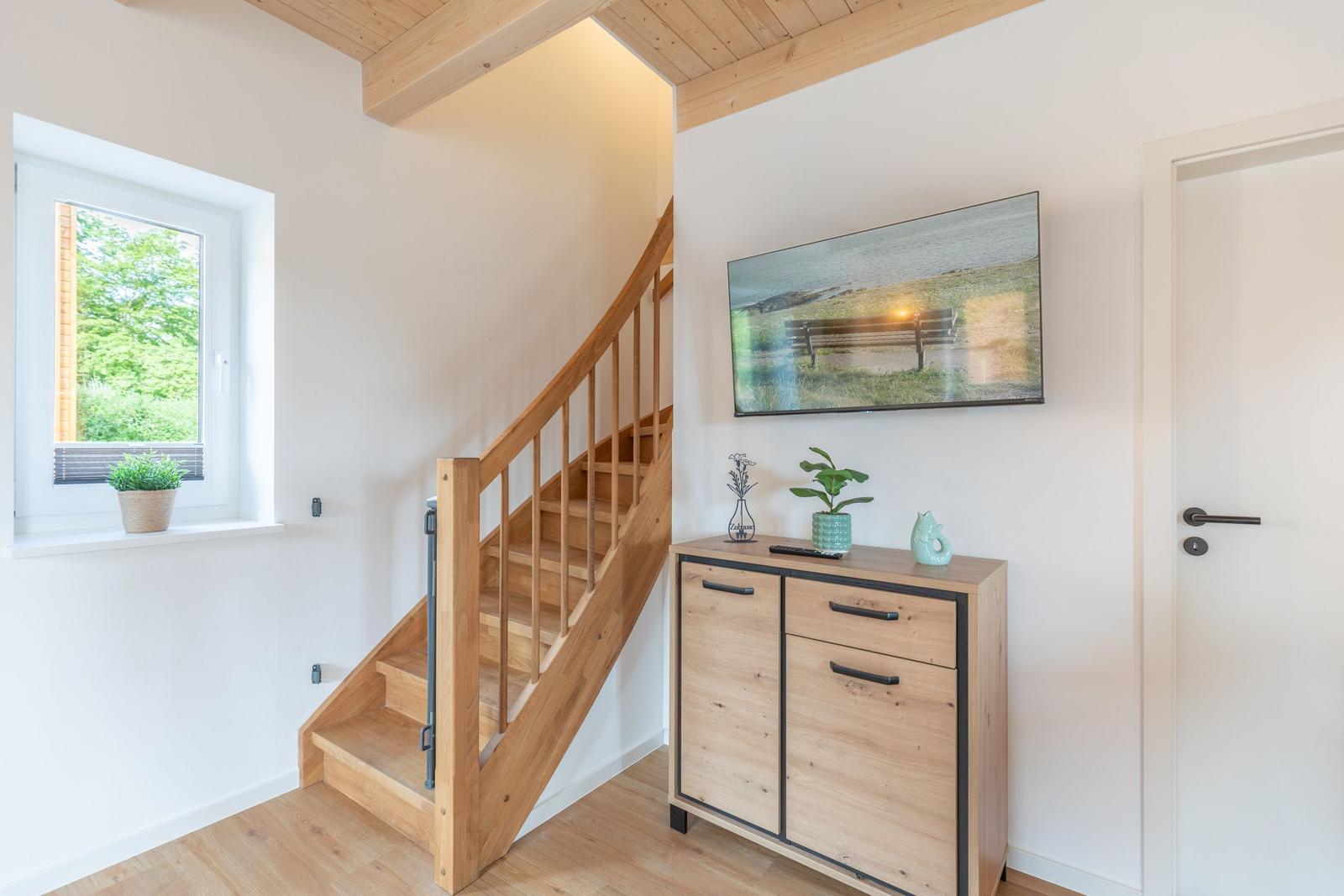 Holztreppe führt zur oberen Etage. Wandbild, Schrank und Fenster sichtbar.