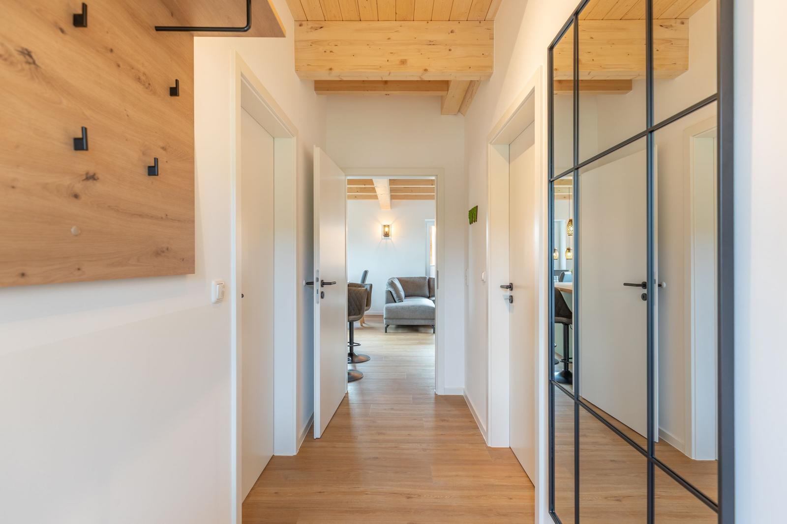 Flur mit Holzboden und Deckenbalken. Türen führen in Wohn- und Essbereich.