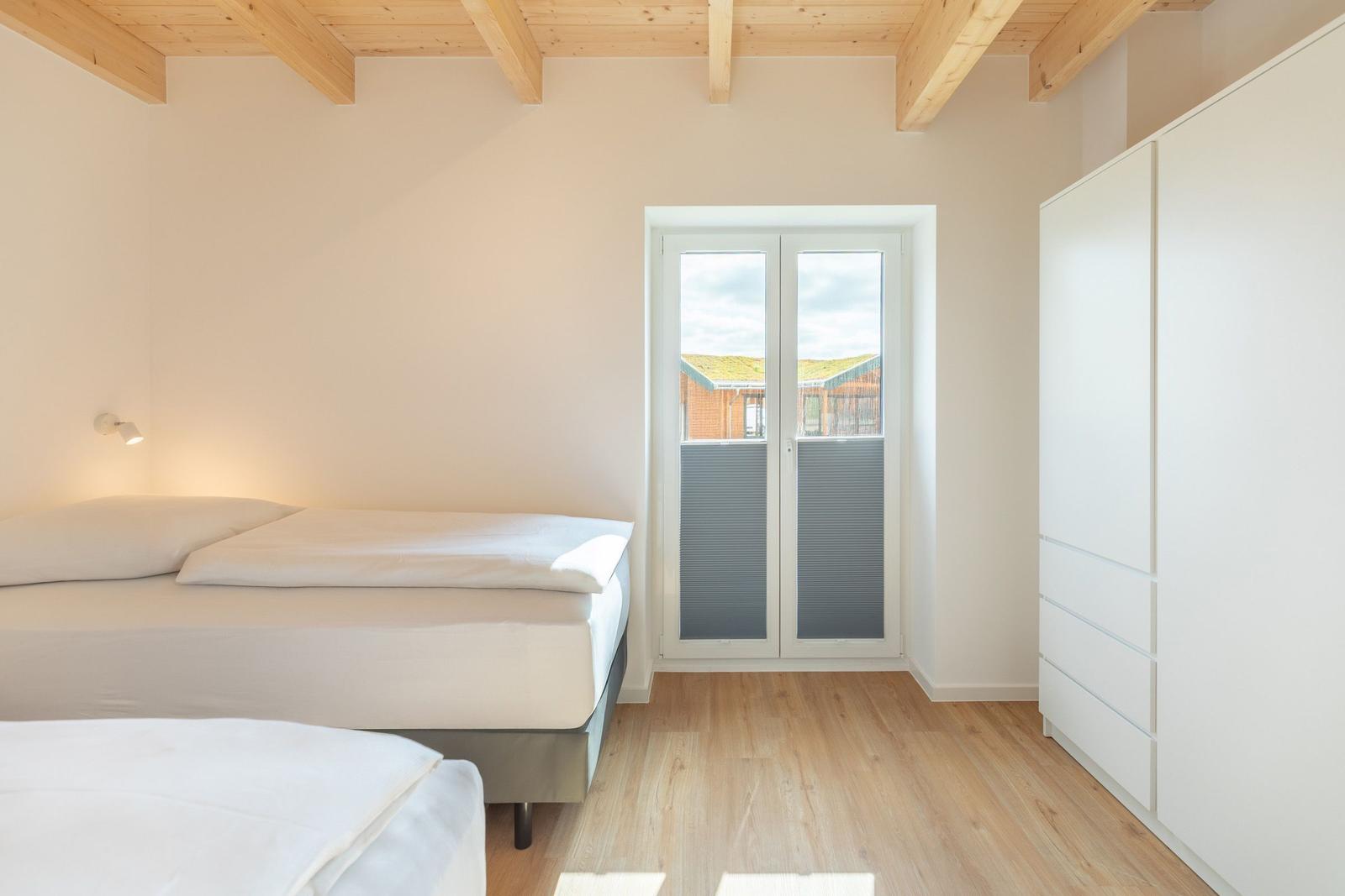 Zimmer mit zwei Betten, Holzdecke und Balkontür.