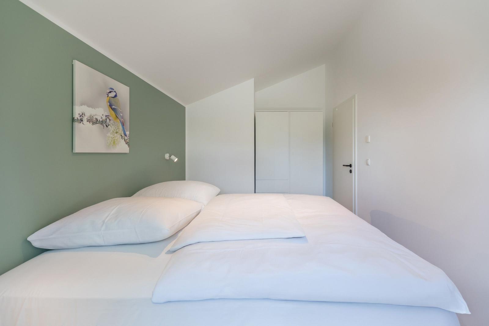 Schlafzimmer mit Bett, Wandbild und Schrank.