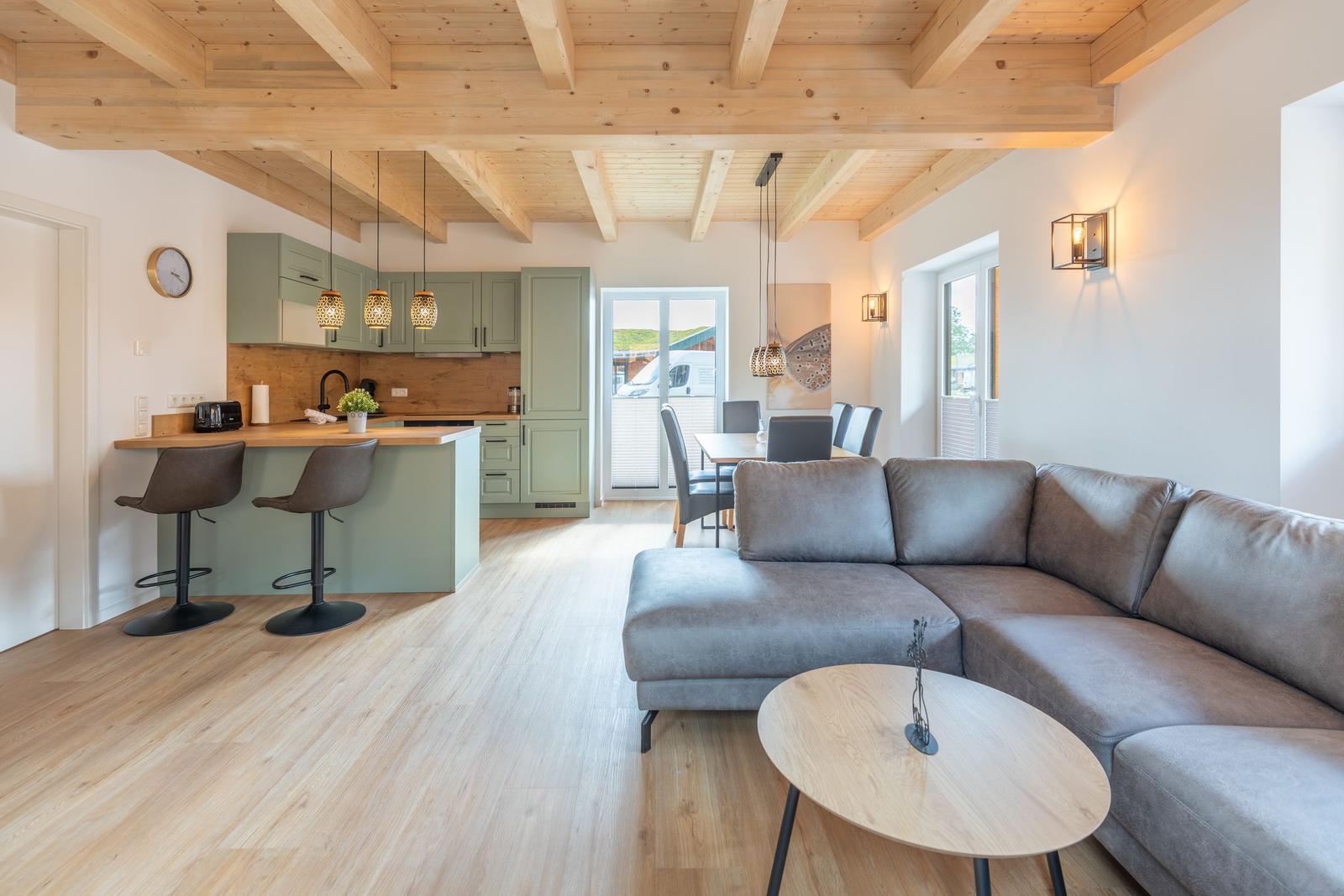 Wohn- und Essbereich mit Kücheninsel und Holzbalkendecke.