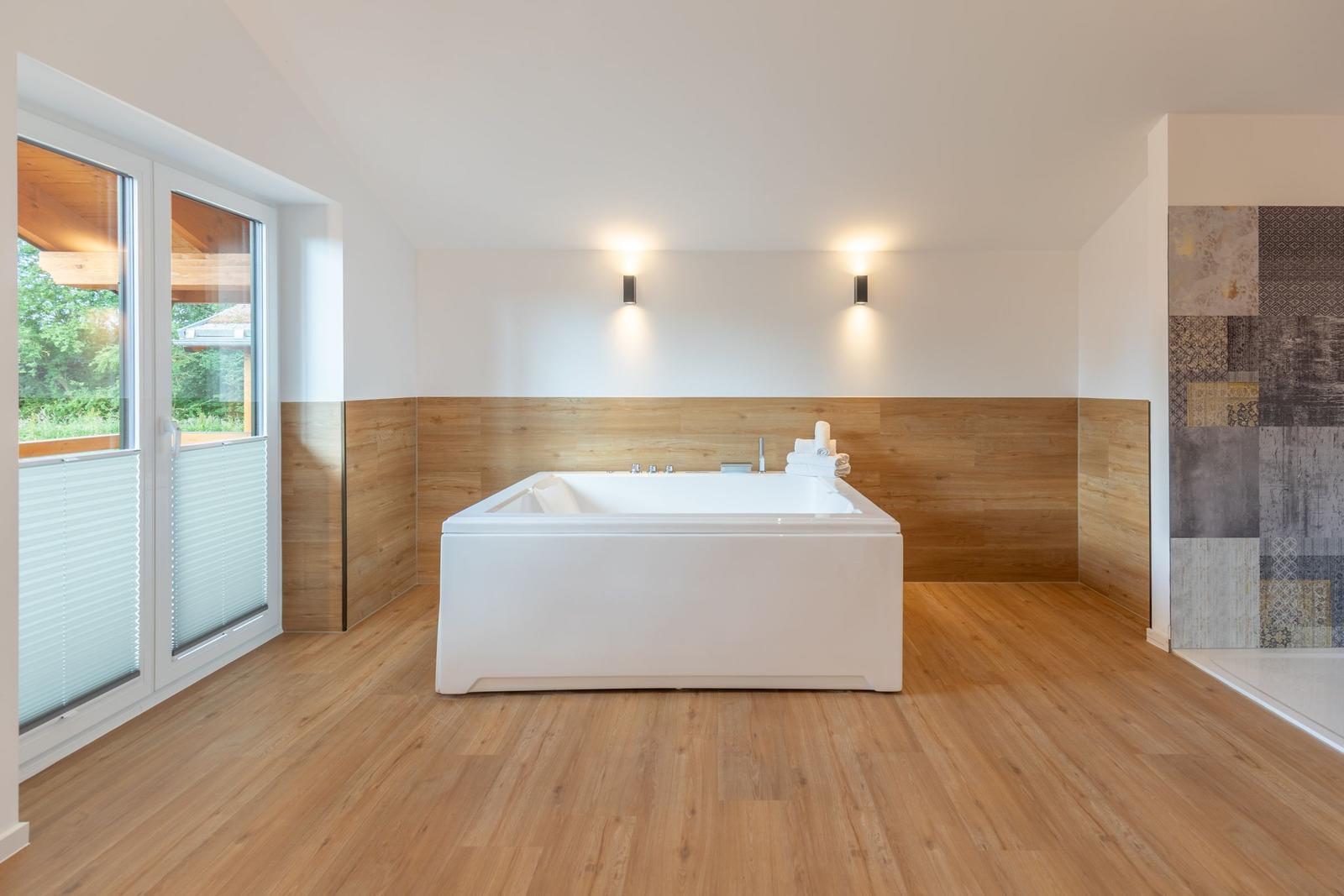 Bad mit Whirlpool, Holzfußboden und großem Fenster zur Terrasse.