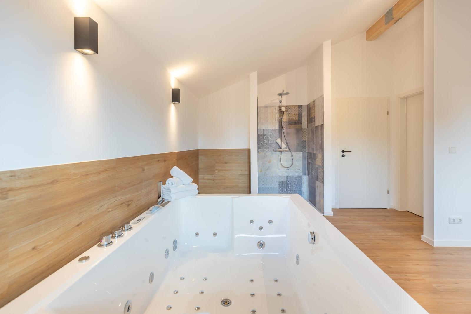 Bad mit Whirlpool und Dusche, Holzverkleidung und moderner Beleuchtung.