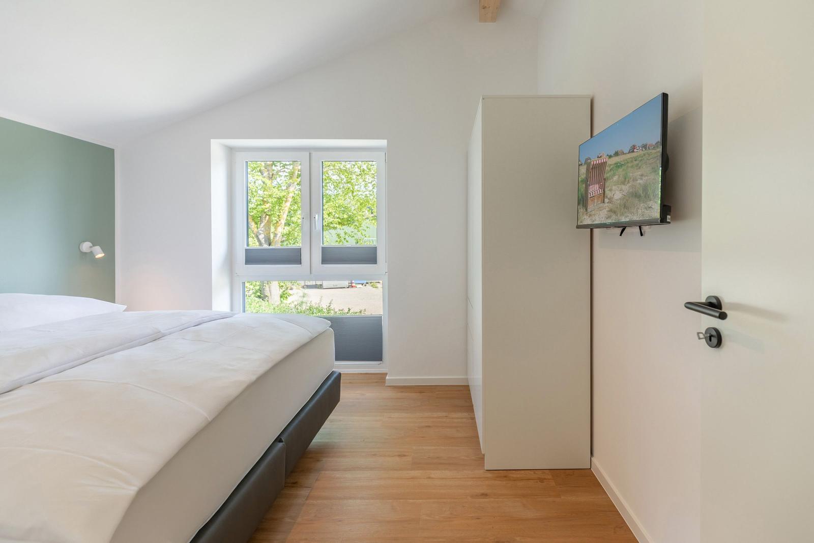 Schlafzimmer mit Bett, Fenster und Wand-TV.