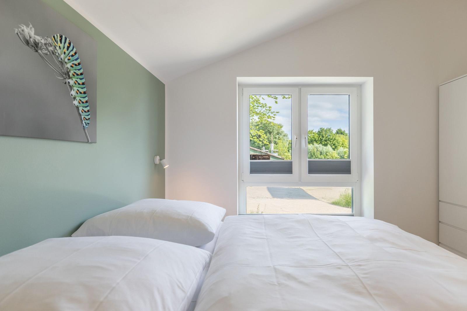 Schlafzimmer mit Bett, Fenster und Wandbild.