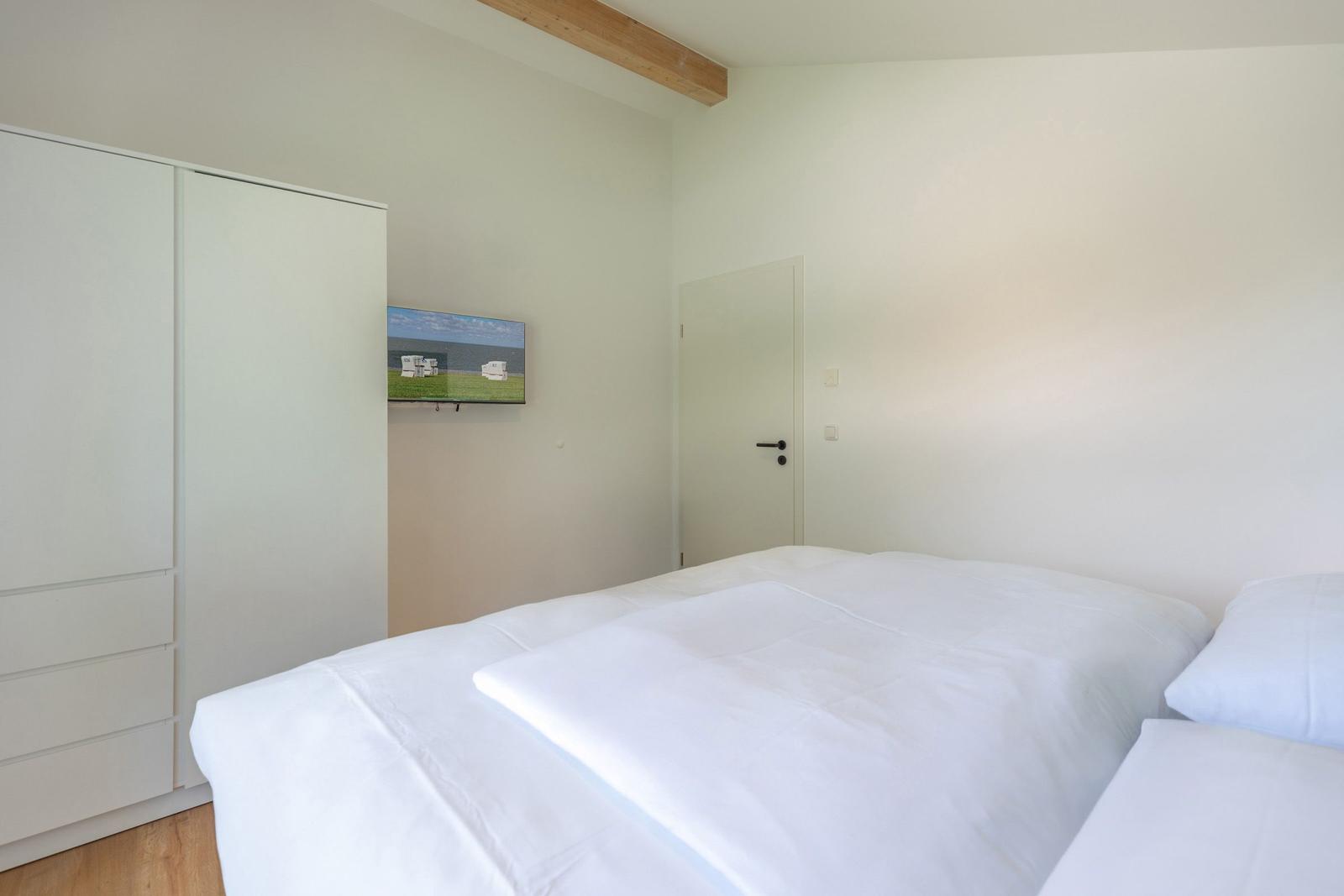 Schlafzimmer mit weißem Bett, Kleiderschrank und Wandbild.