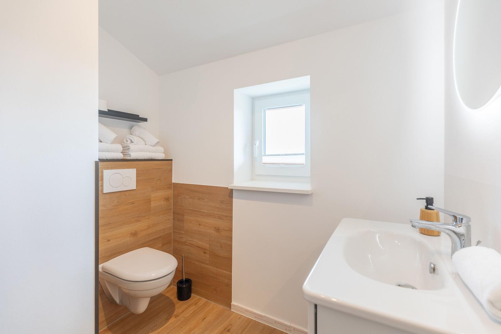 Badezimmer mit Toilette, Waschbecken und kleinem Fenster.