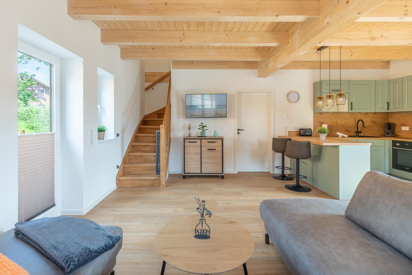 Wohnbereich mit Küchenzeile, Treppenhaus und TV. Holzboden und Deckenbalken.