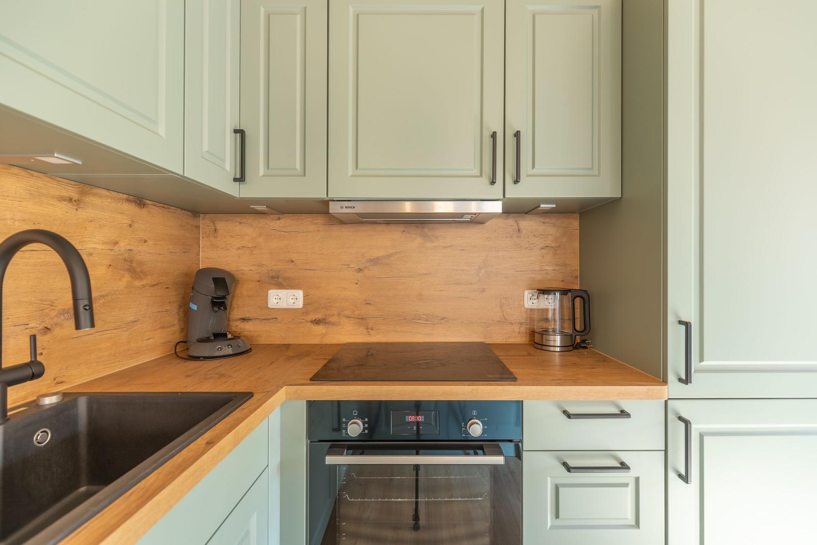 Küche mit Holzoberfläche, grünen Schränken und Edelstahlgeräten.