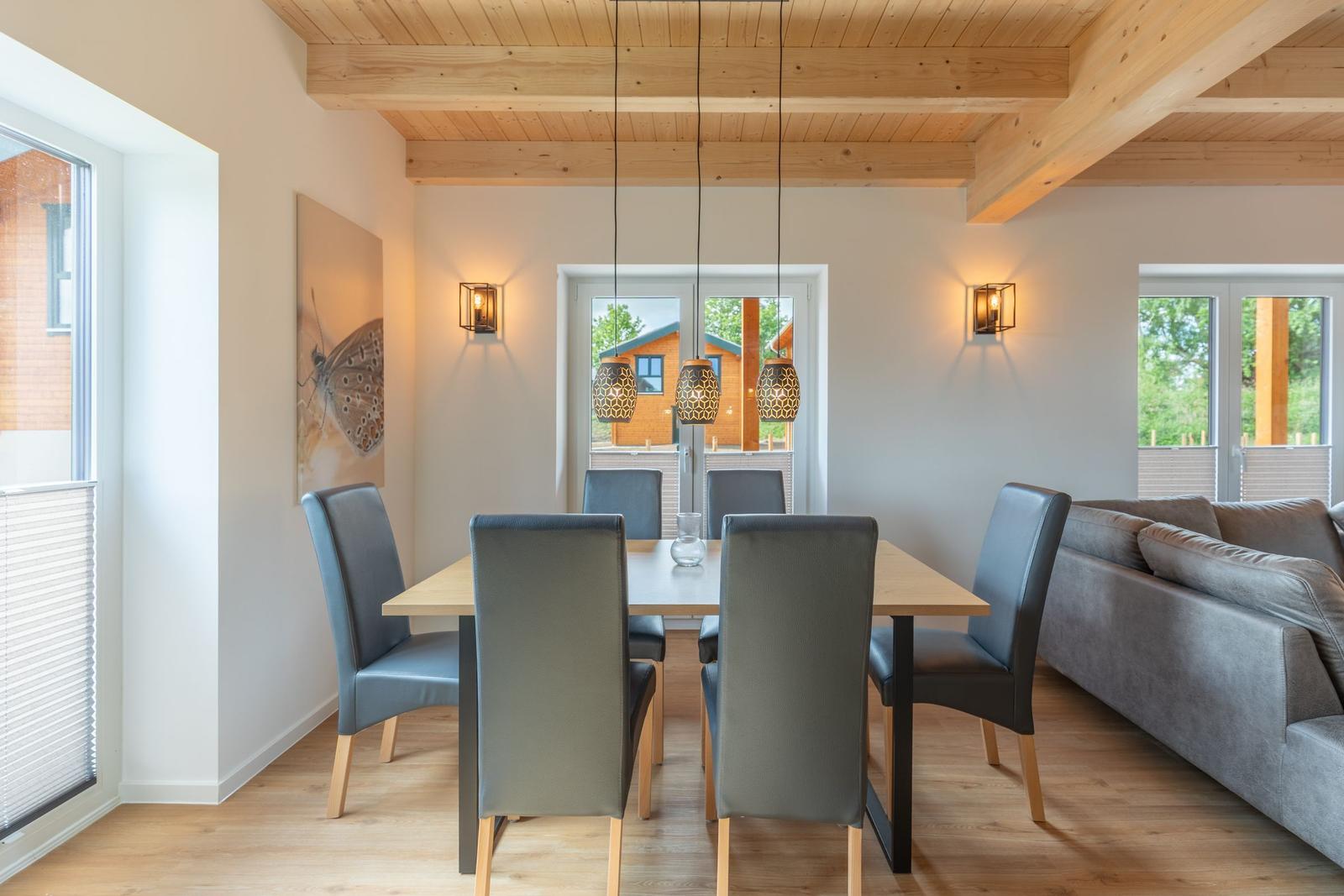 Esszimmer mit Tisch, Stühlen und Sofa. Holzdecke und große Fenster.