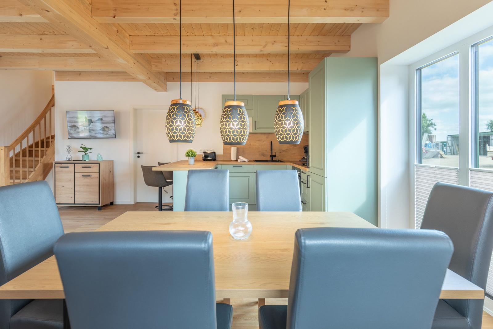 Essbereich mit Holztisch und blauen Stühlen unter Holzbalkendecke.