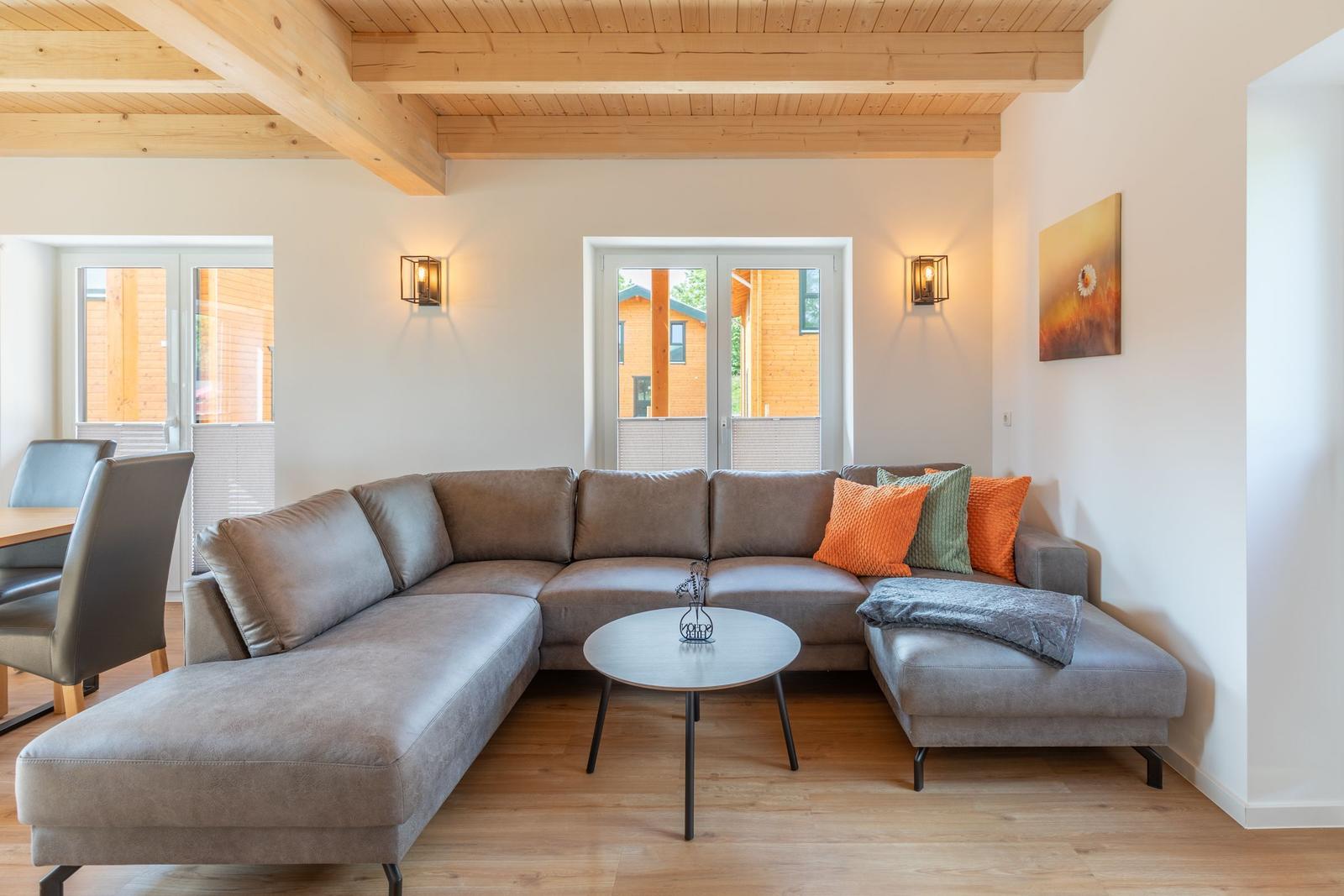 Wohnzimmer mit grauem Sofa, Holzdecke und Blick auf Balkon.