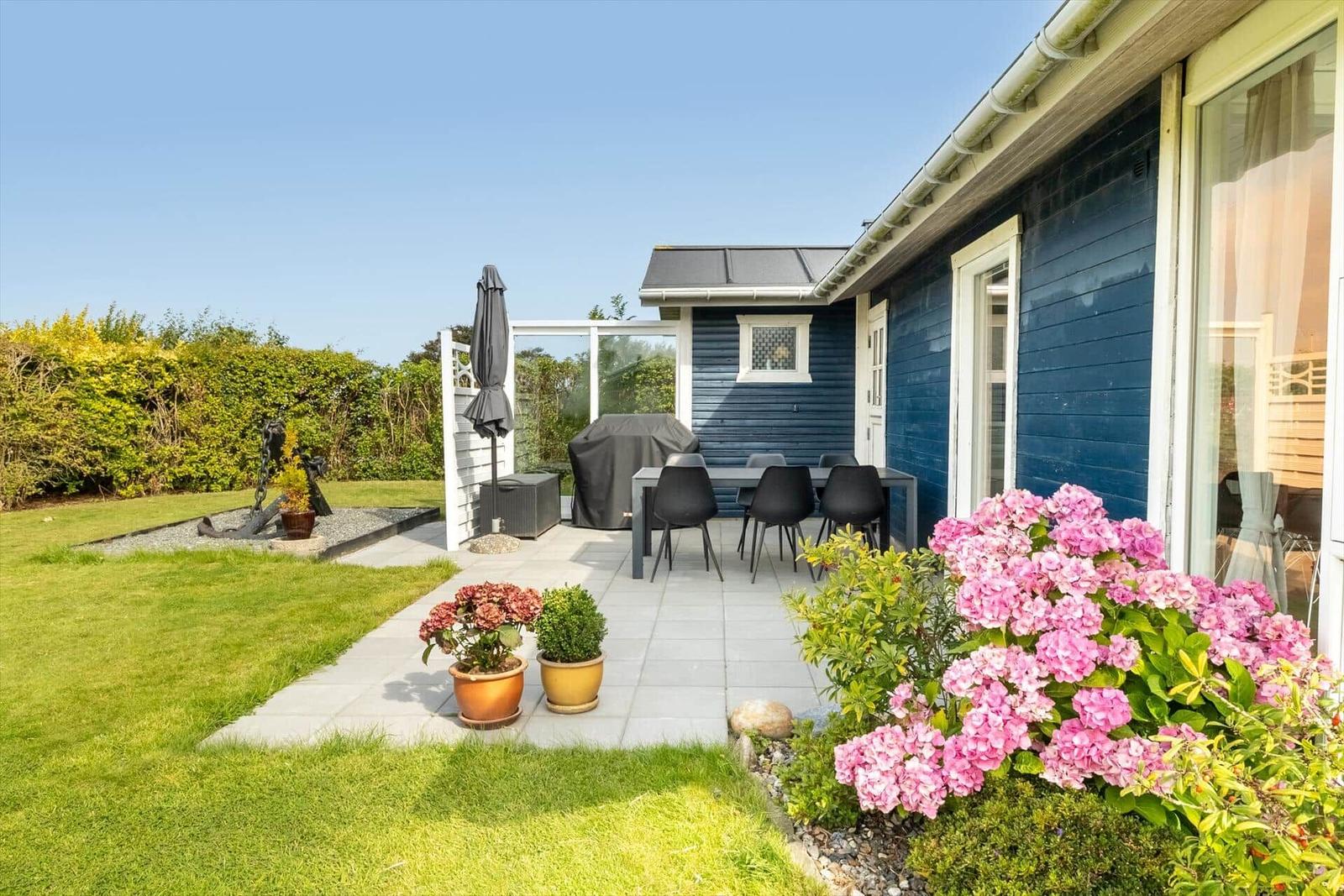 Terrace with table, chairs, and grill. Blooming garden with flowers and lawn.