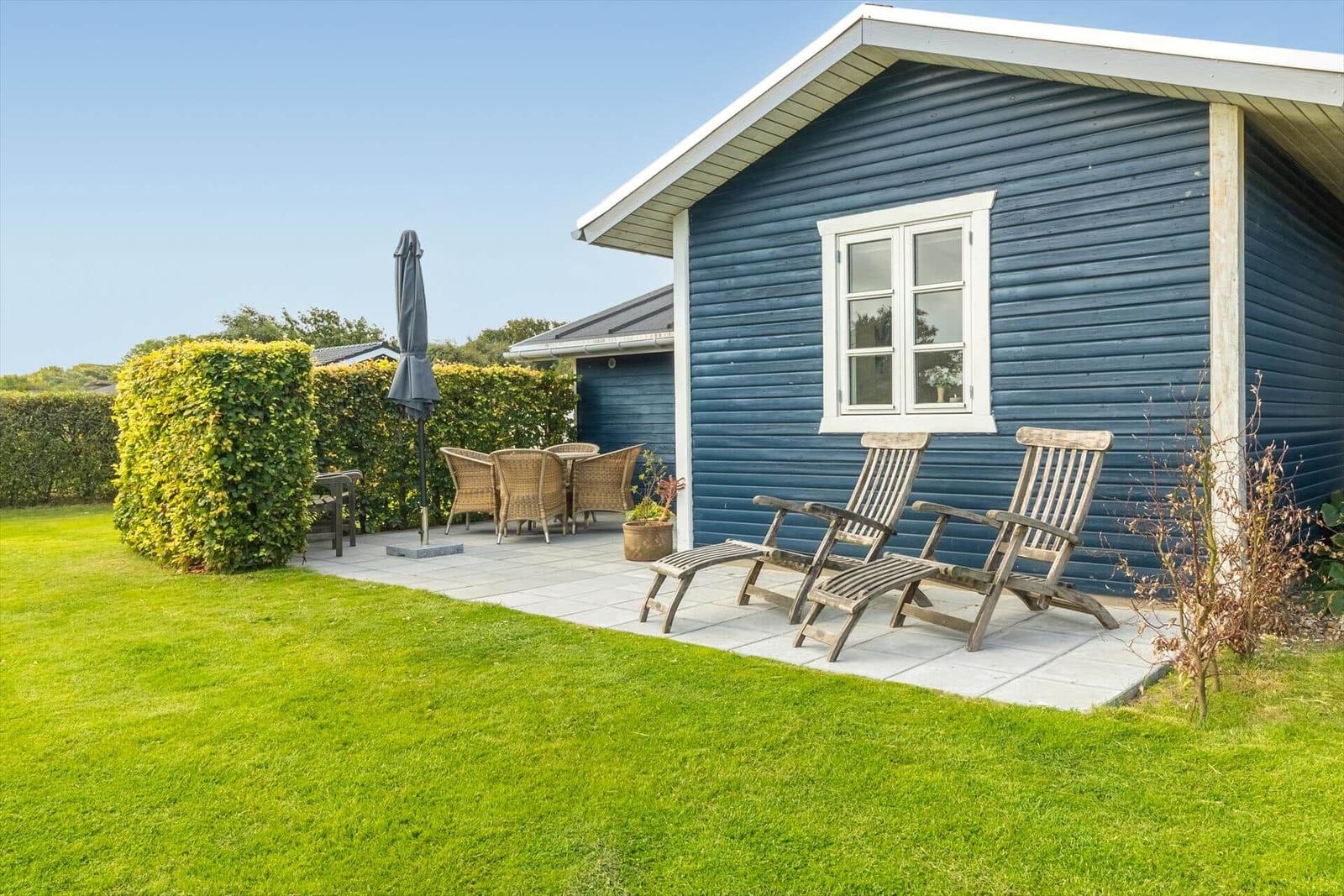 Blue wooden cabin with terrace, wooden chairs, and green lawn.