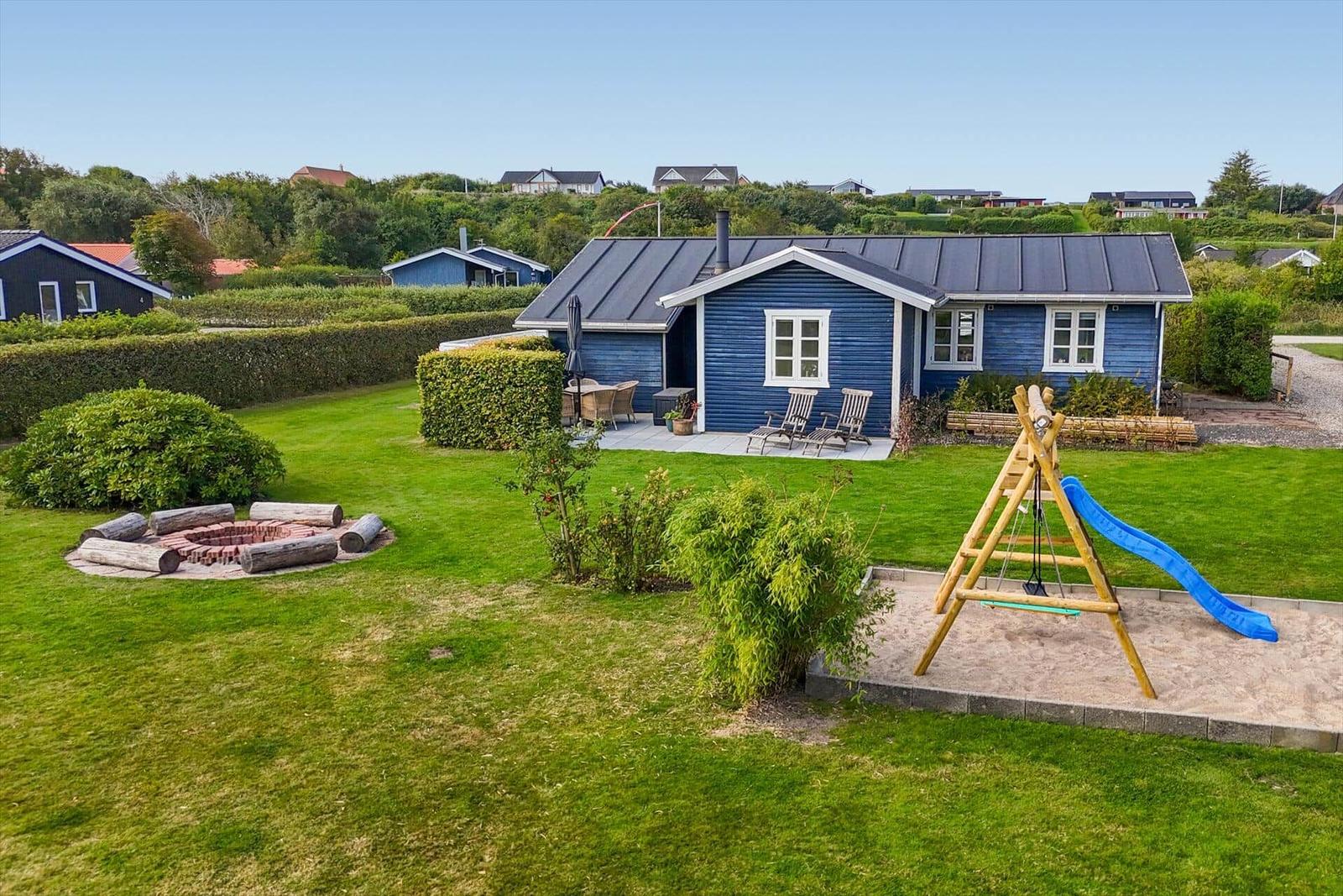 Blue wooden house with garden, playground, and fire pit.