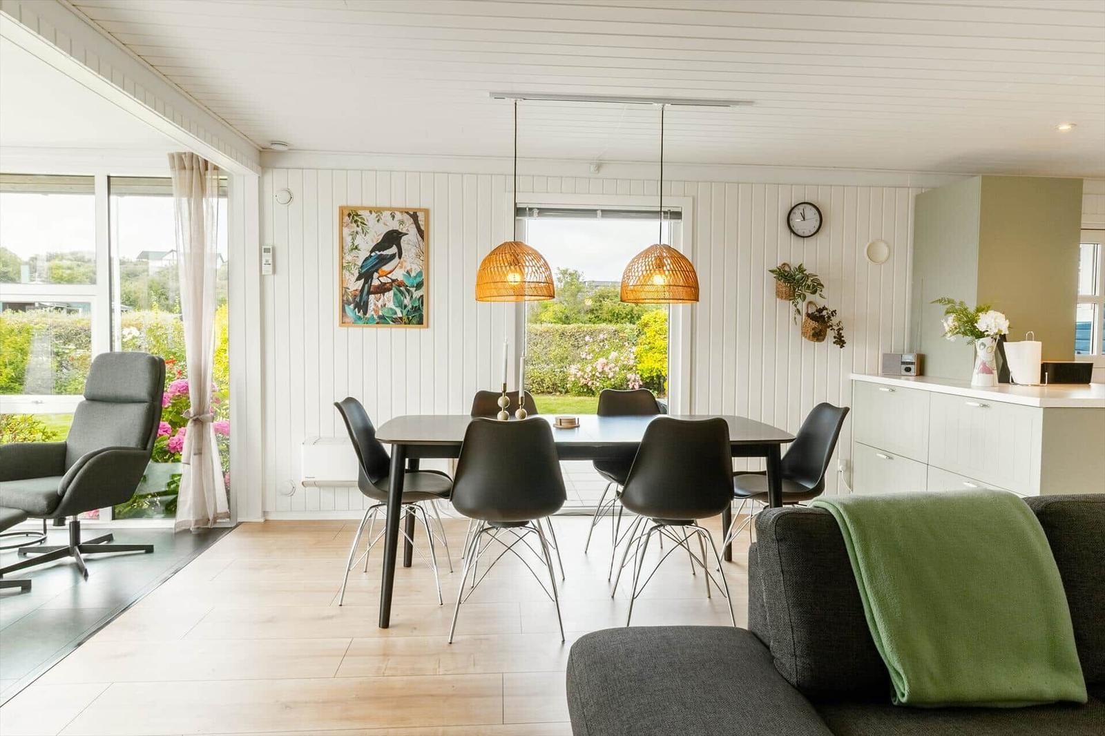 Dining area with table, chairs, and pendant lights. View of garden through windows.