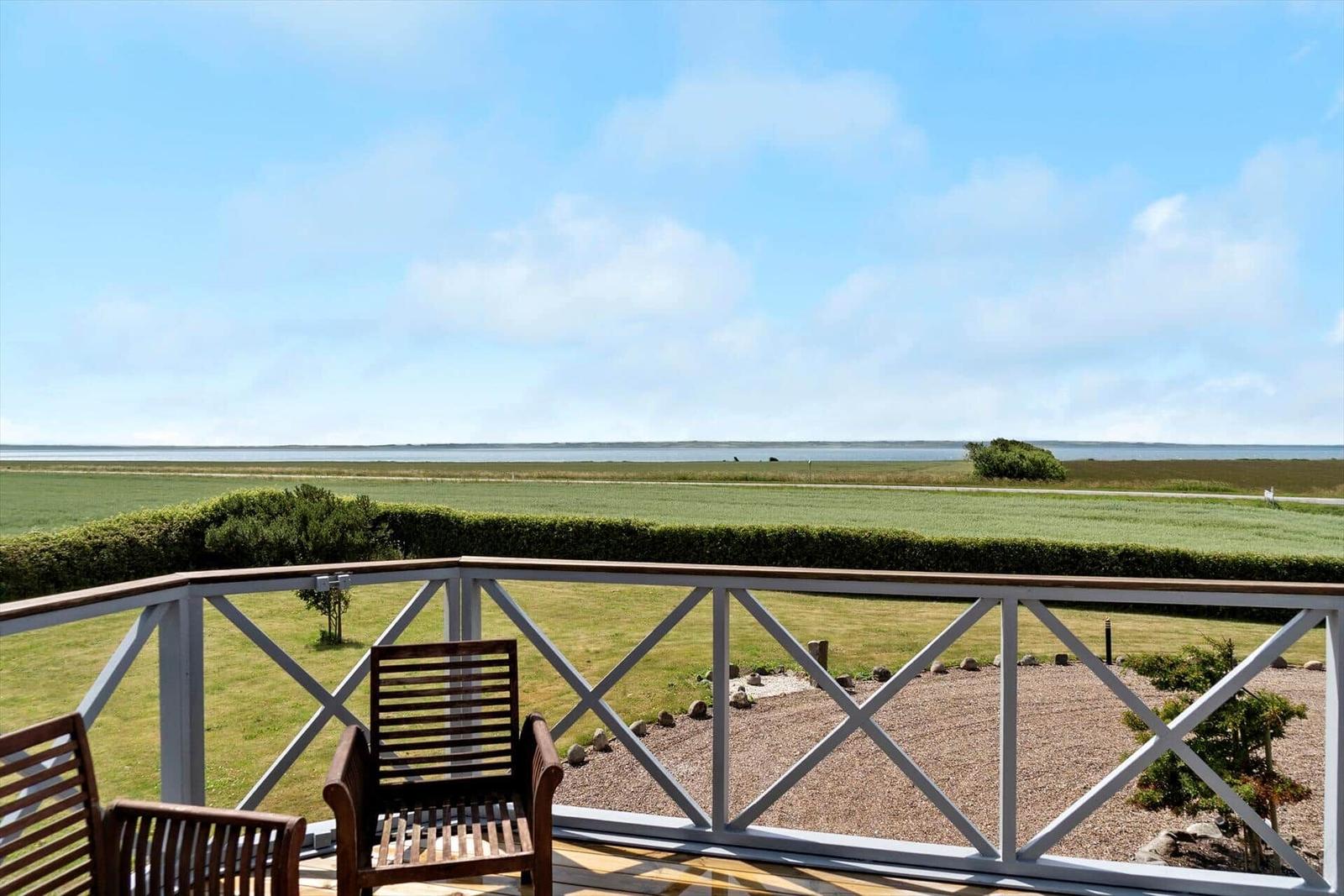 Deck with wooden chairs and view of fields and water.