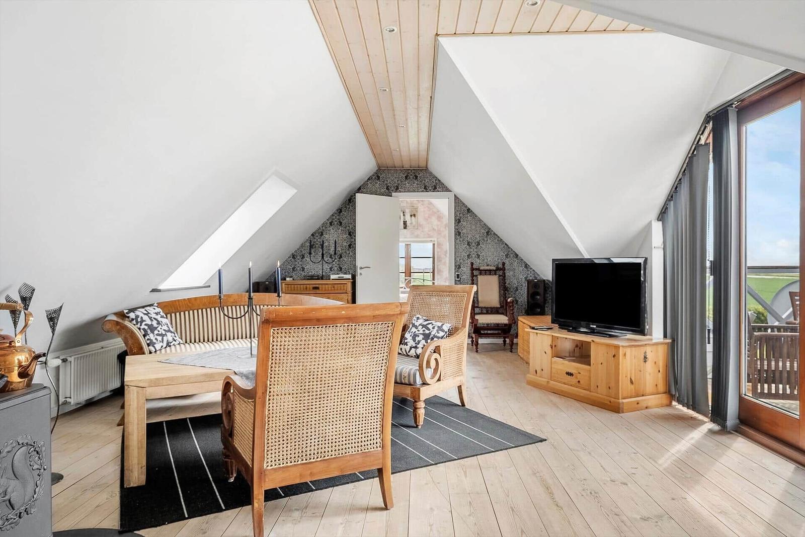 Living room with wooden floor, TV, and seating under sloped ceilings.