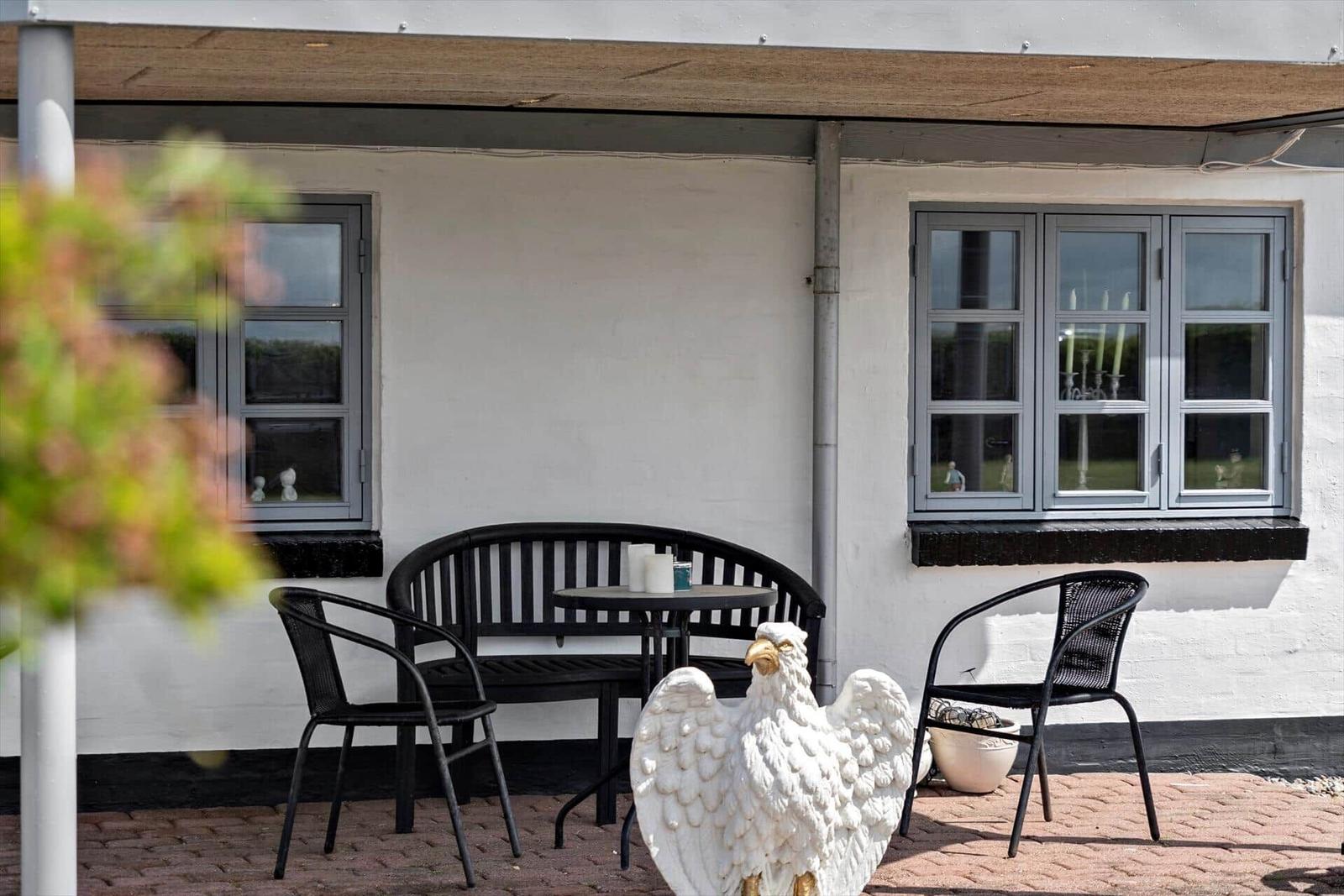 Terrace with table, two chairs, and a white bird statue against white wall.