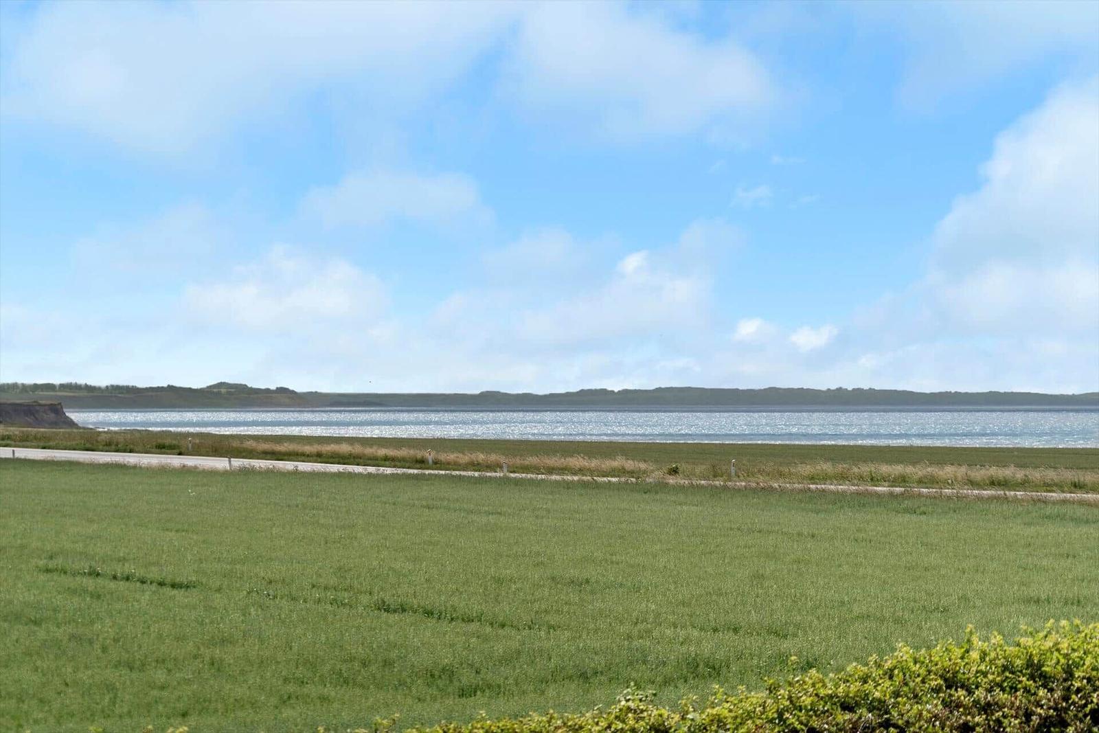 Vast grassy area with view of a lake under blue sky.
