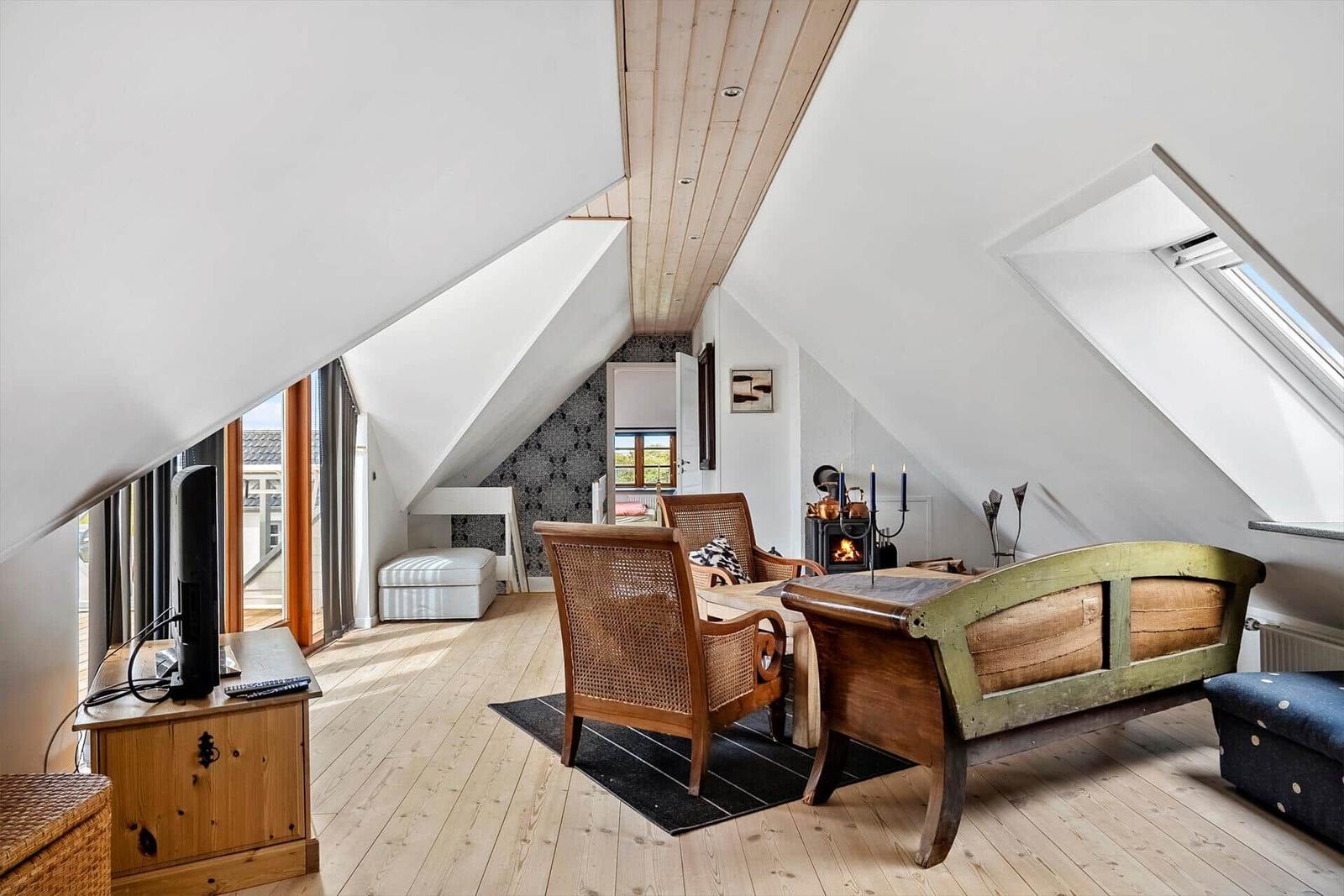 Attic apartment with wooden floor, seating, and wood stove.