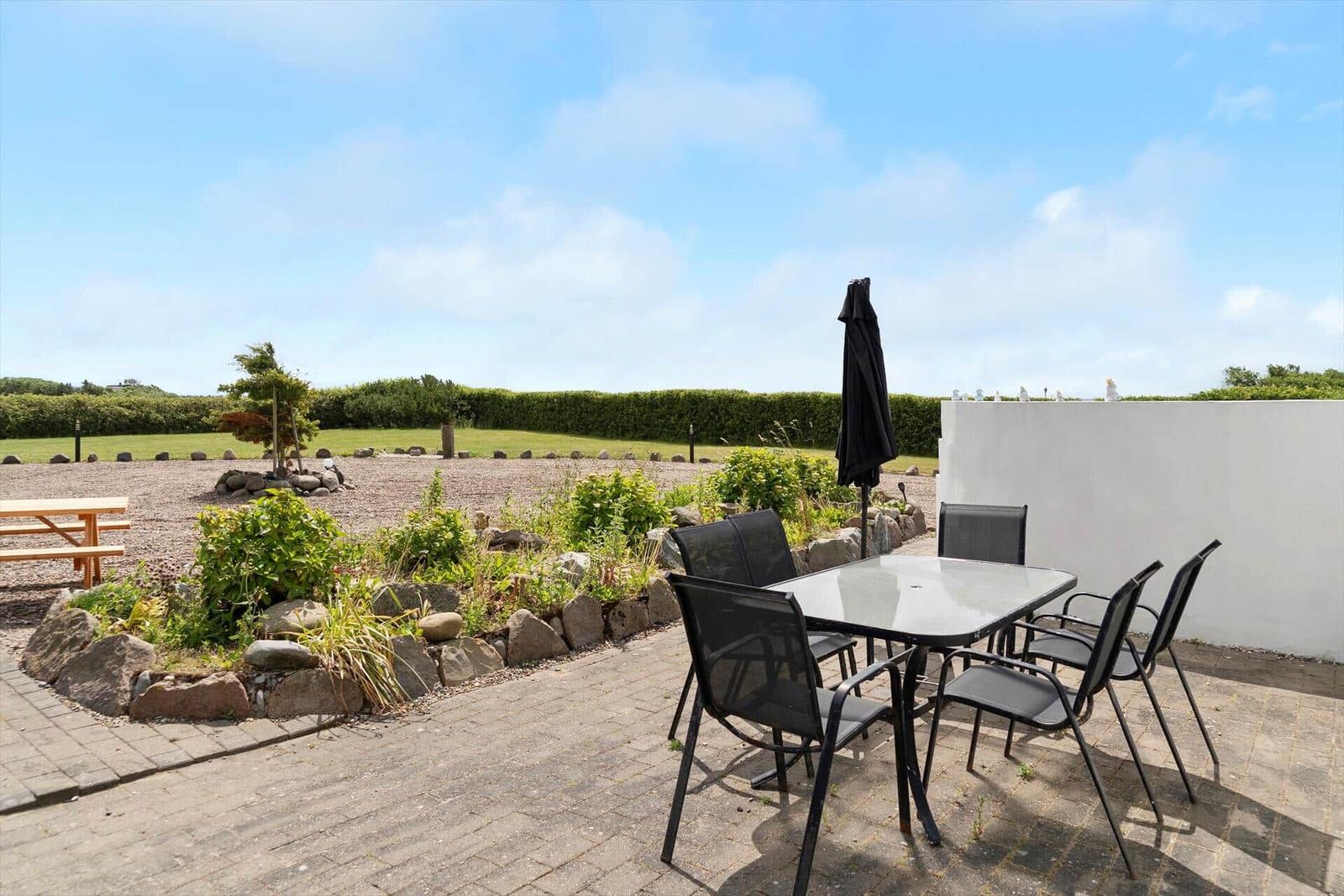 Terrace with table, chairs, and umbrella. Garden area with stones and greenery.