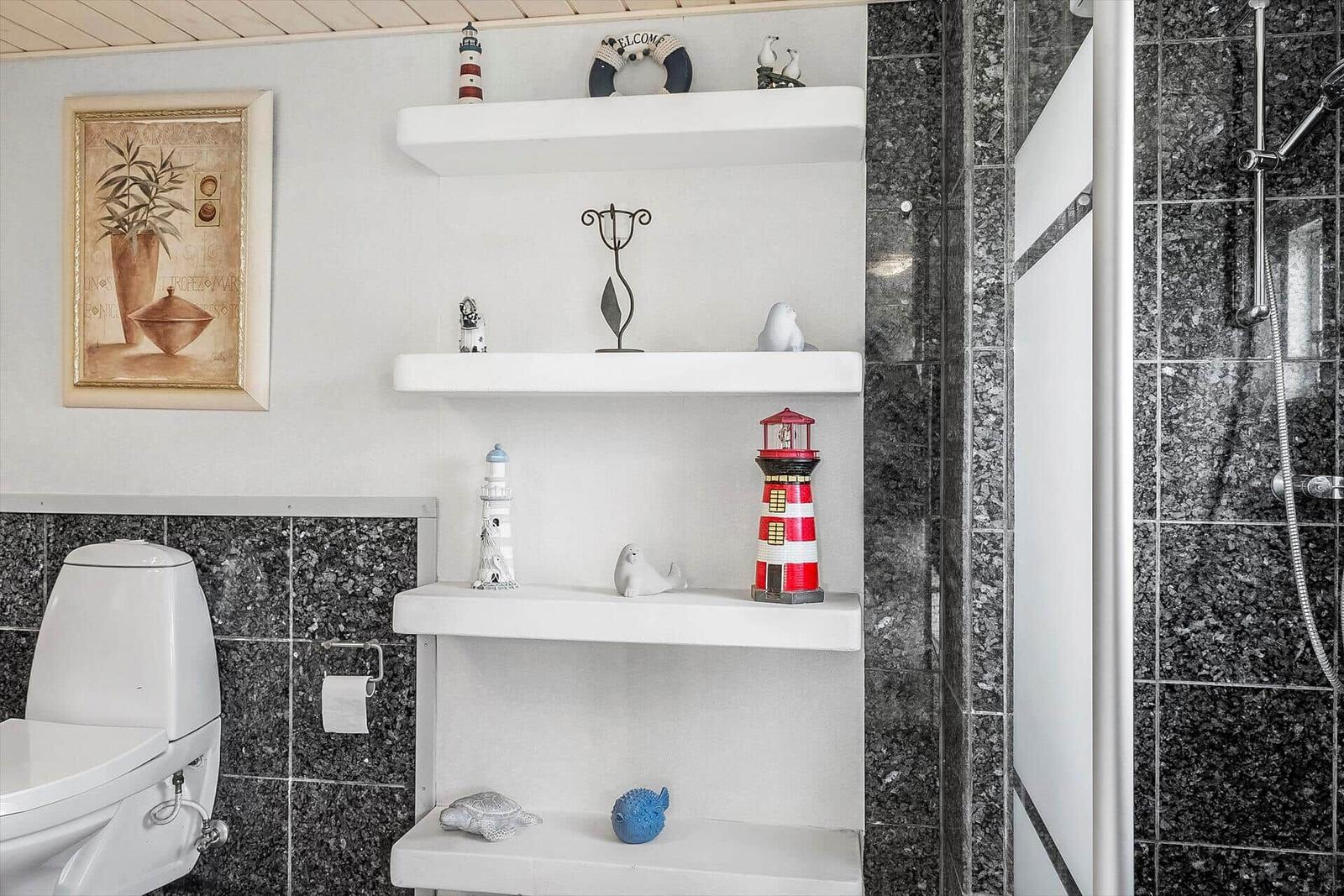 Bathroom with shower, toilet, and shelves with seal and lighthouse figurines.