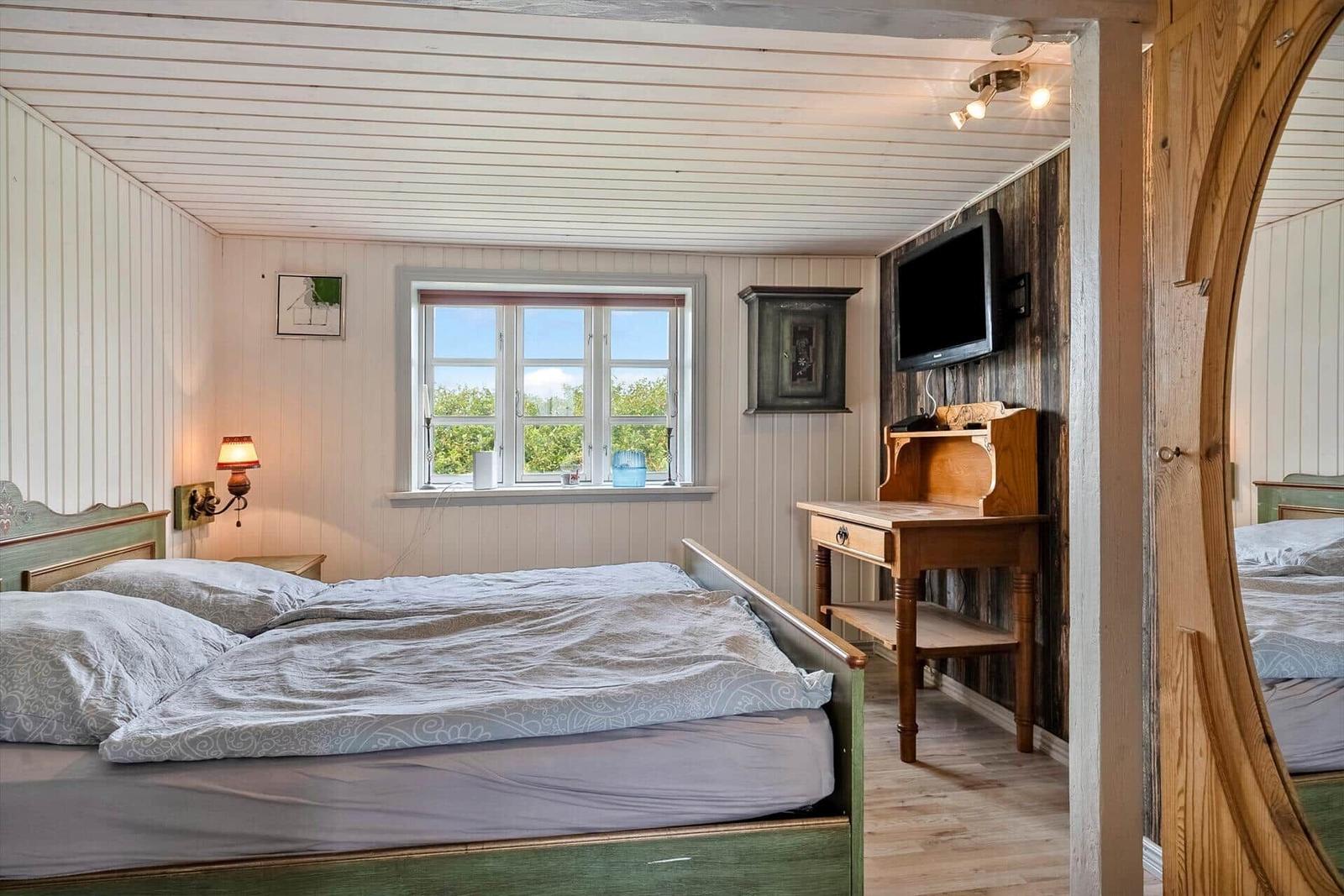 Bedroom with bed, desk, and window with view of greenery.