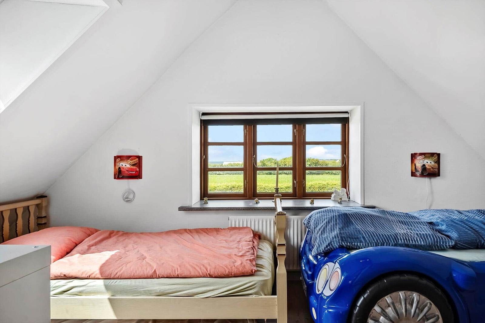 Room with sloped ceiling, window, and two beds.