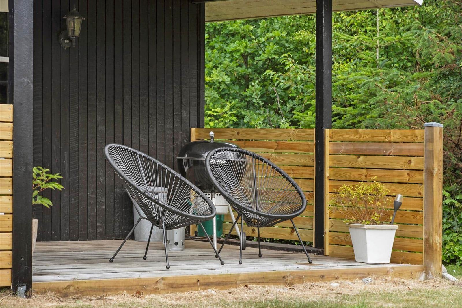 Deck with two chairs, grill, and plants. Background: green trees.