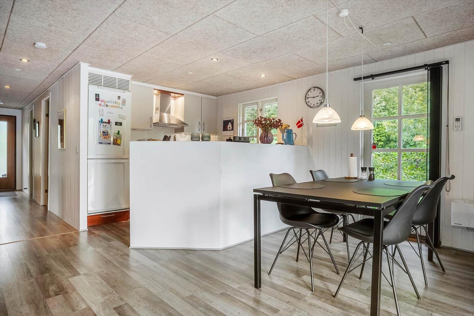 Kitchen with dining area, white worktop, wooden floor, and windows overlooking greenery.
