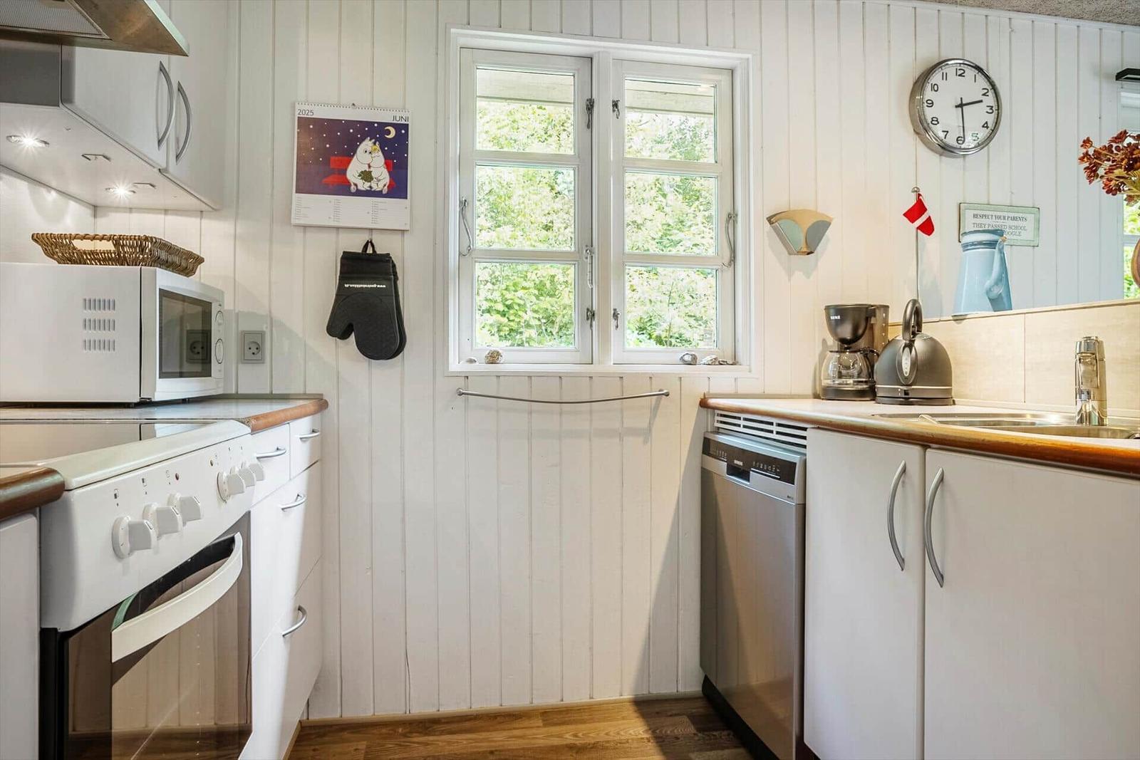 Kitchen with white cabinets, stove, dishwasher, and window with view of greenery.