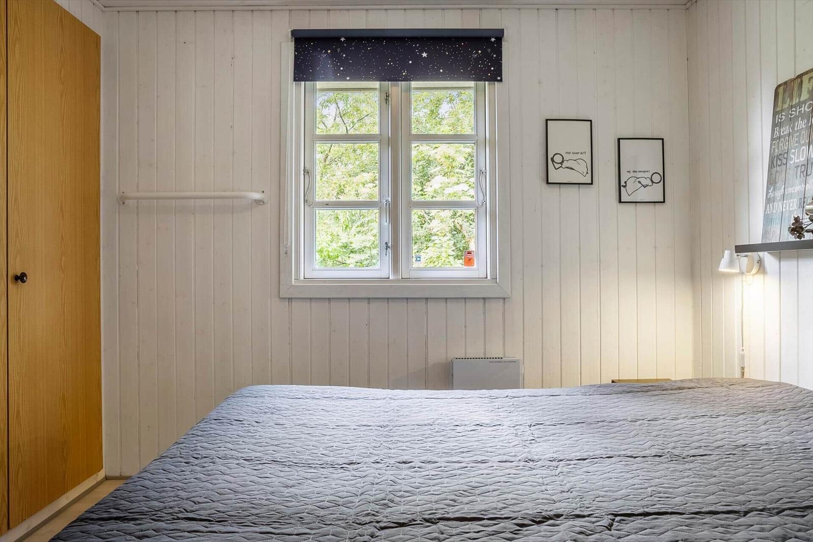 Bedroom with bed, window, and wooden closet against the wall.