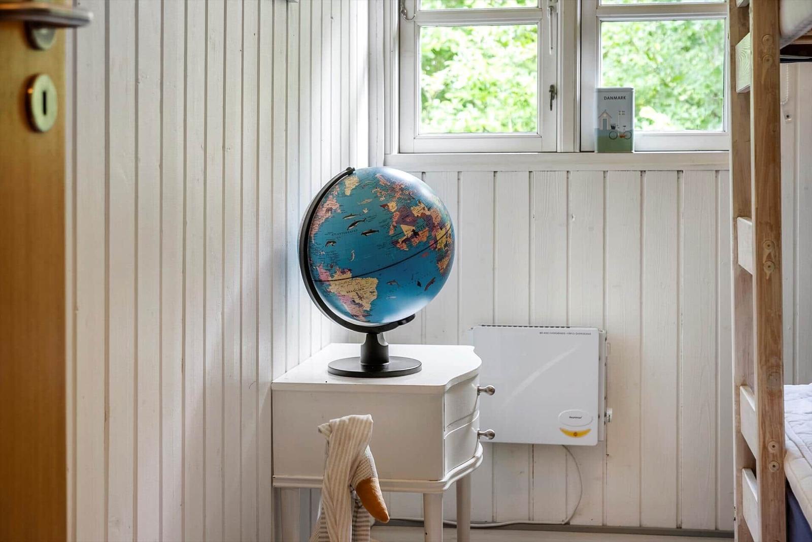 A globe sits on a white nightstand beside a window with a view of greenery.