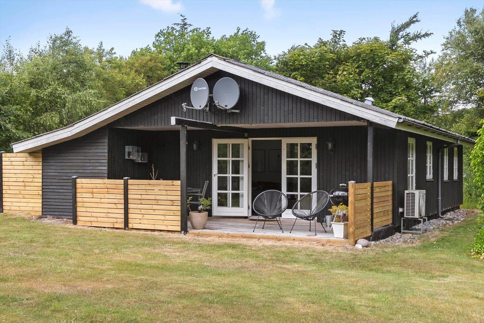Black wooden house with terrace, seating, and satellite dishes.