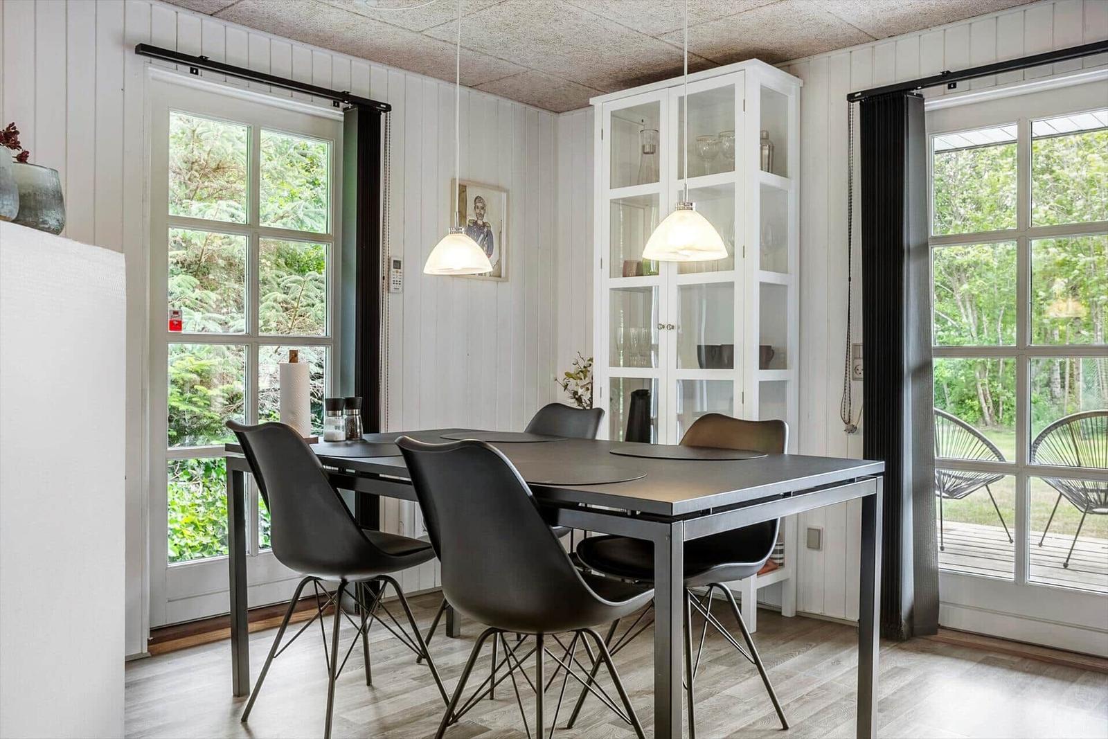 Dining area with table, chairs, and glass cabinet. Windows show garden.