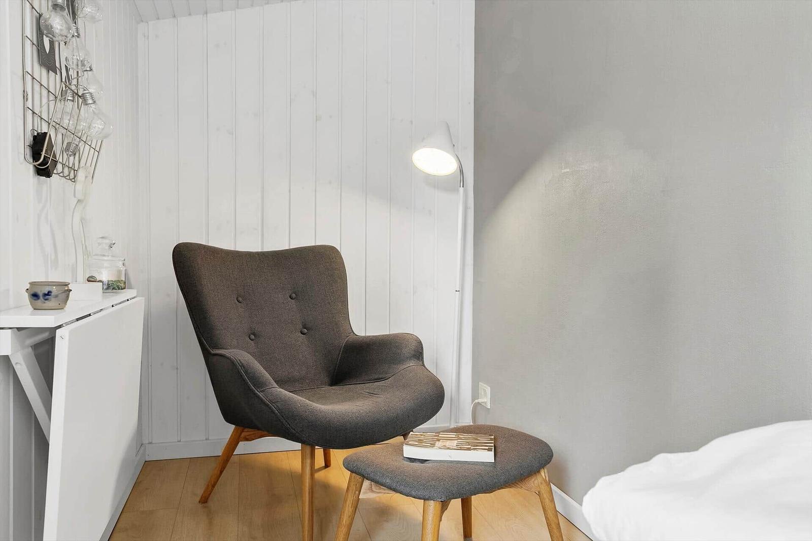 Ein Raum mit grauer Sessel, Beistelltisch und Stehlampe an weißer Wand.