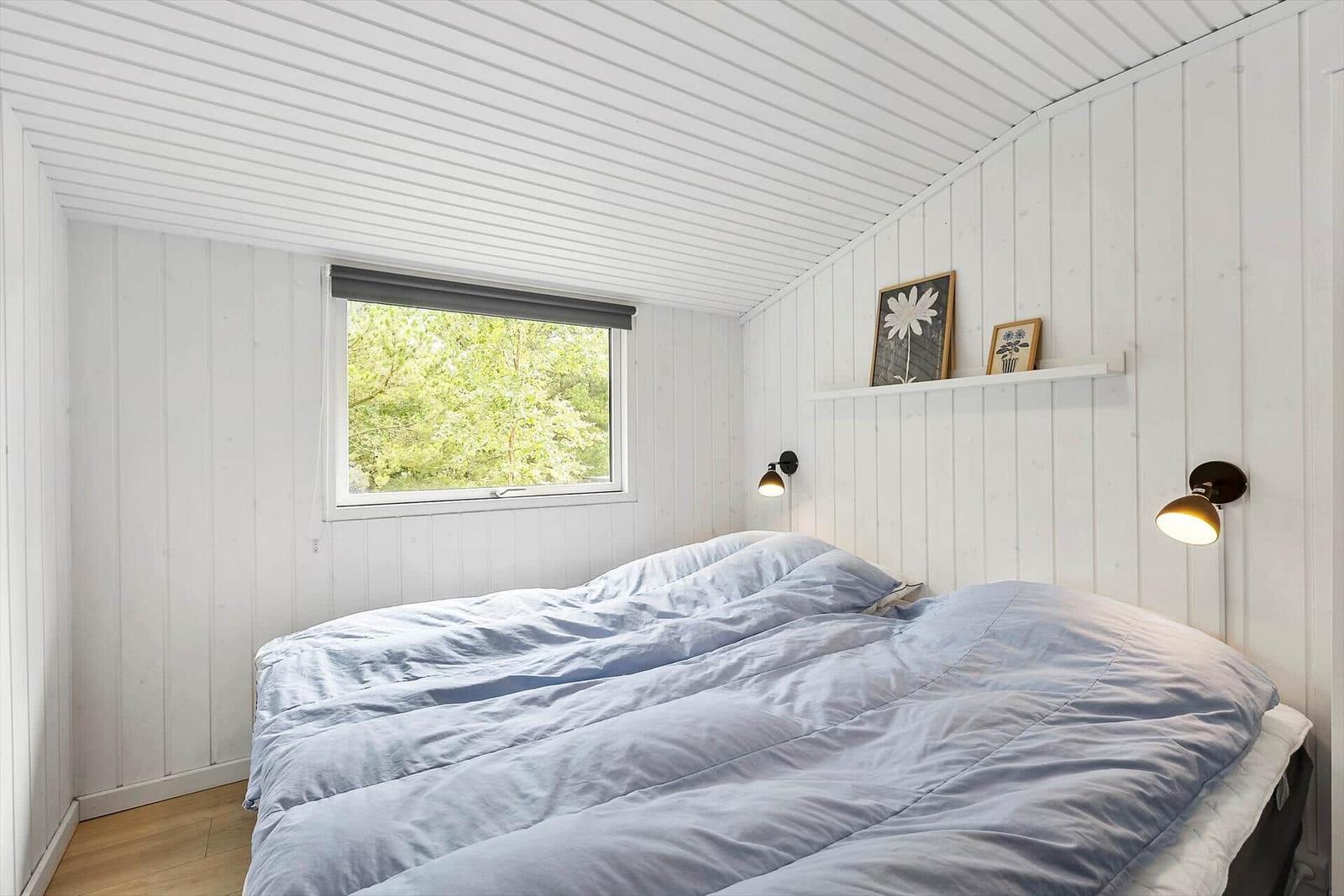 Schlafzimmer mit Bett, Fenster und Wandlampen. Weiße Holzwandverkleidung.