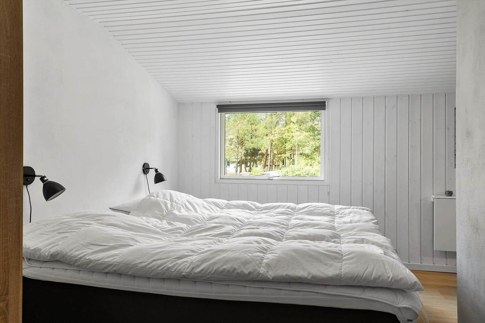Schlafzimmer mit großem Bett, Fenster mit Waldblick und Wandlampen.