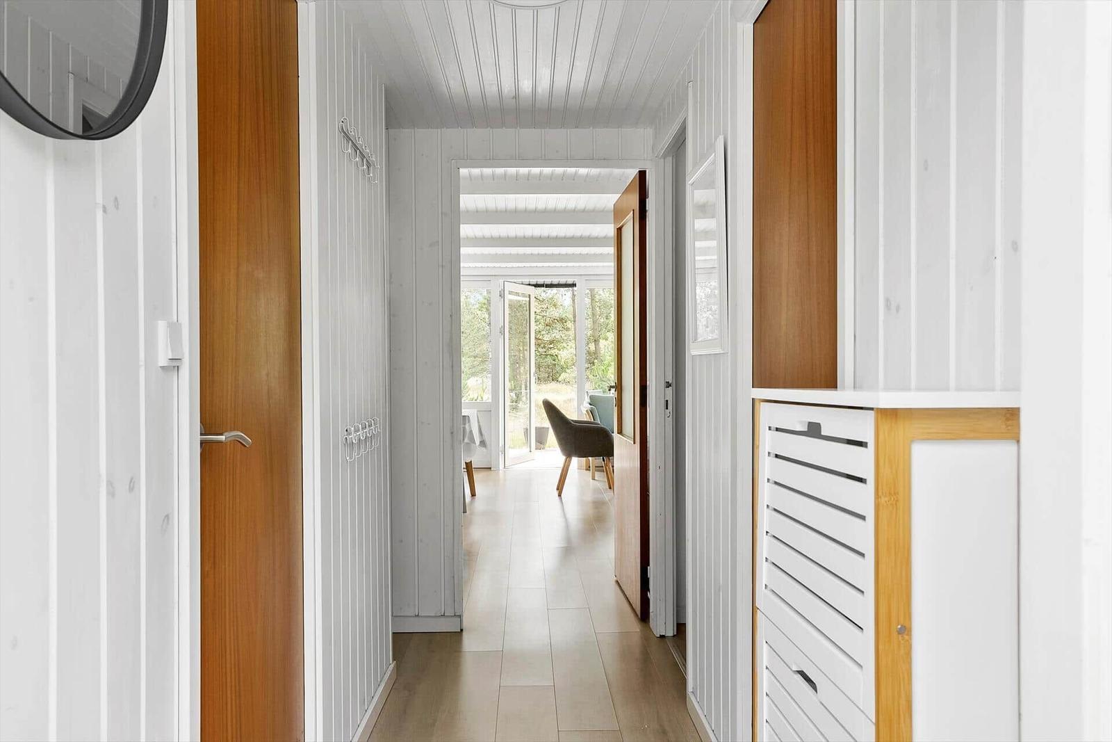 Flur mit weißen Wänden und Holztüren führt zu einem hellen Raum mit Fenster.