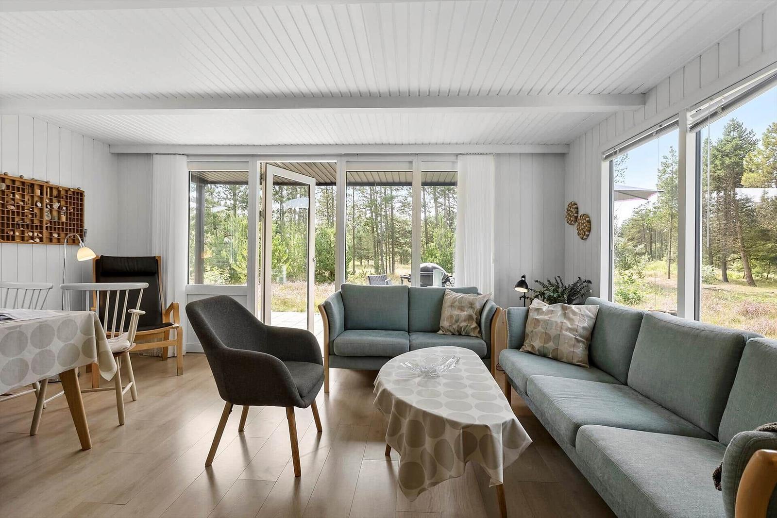 Wohnzimmer mit Sofa, Stühlen und Blick auf Wald.