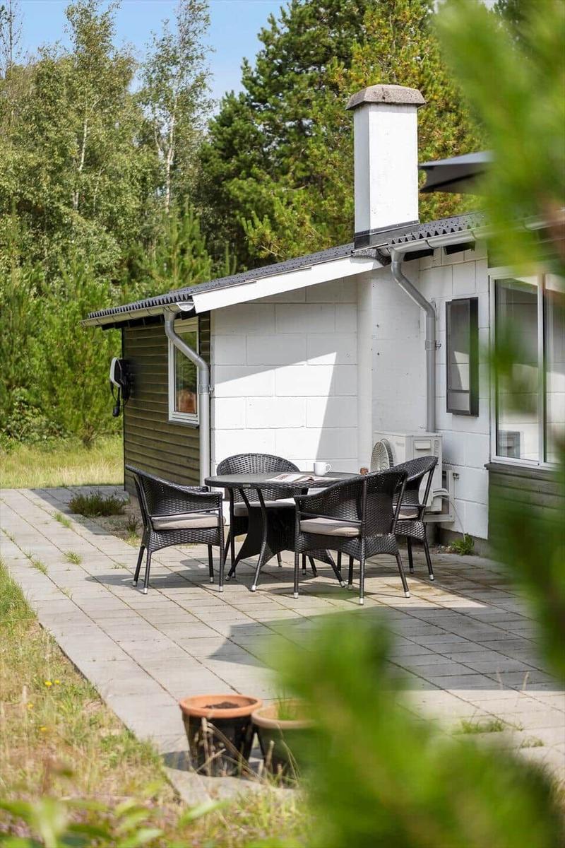 Terrasse mit Tisch und Stühlen vor einem Haus mit weißen Wänden und Schornstein.