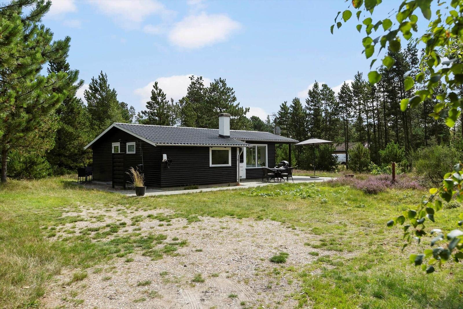 Schwarzes Holzhaus mit Terrasse und Grillplatz im Wald