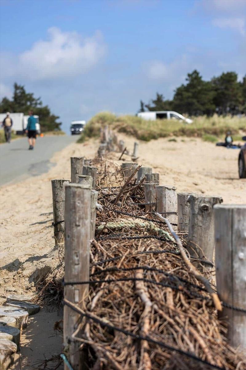 Holzpfostenzaun mit Sträuchern entlang einer Sandstraße