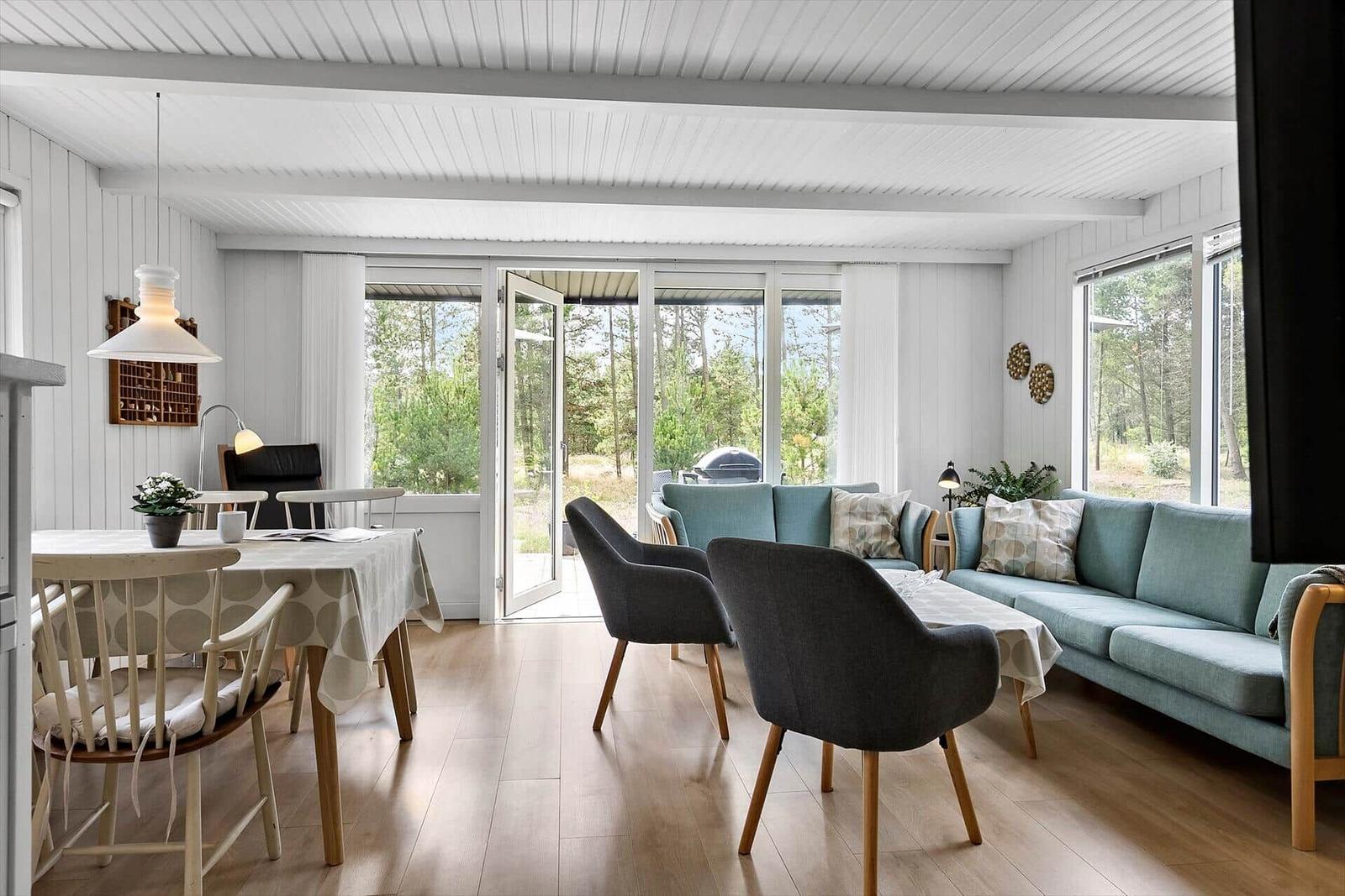 Wohn- und Essbereich mit Sofa, Stühlen und Tisch. Durchgang zur Terrasse mit Blick in den Wald.